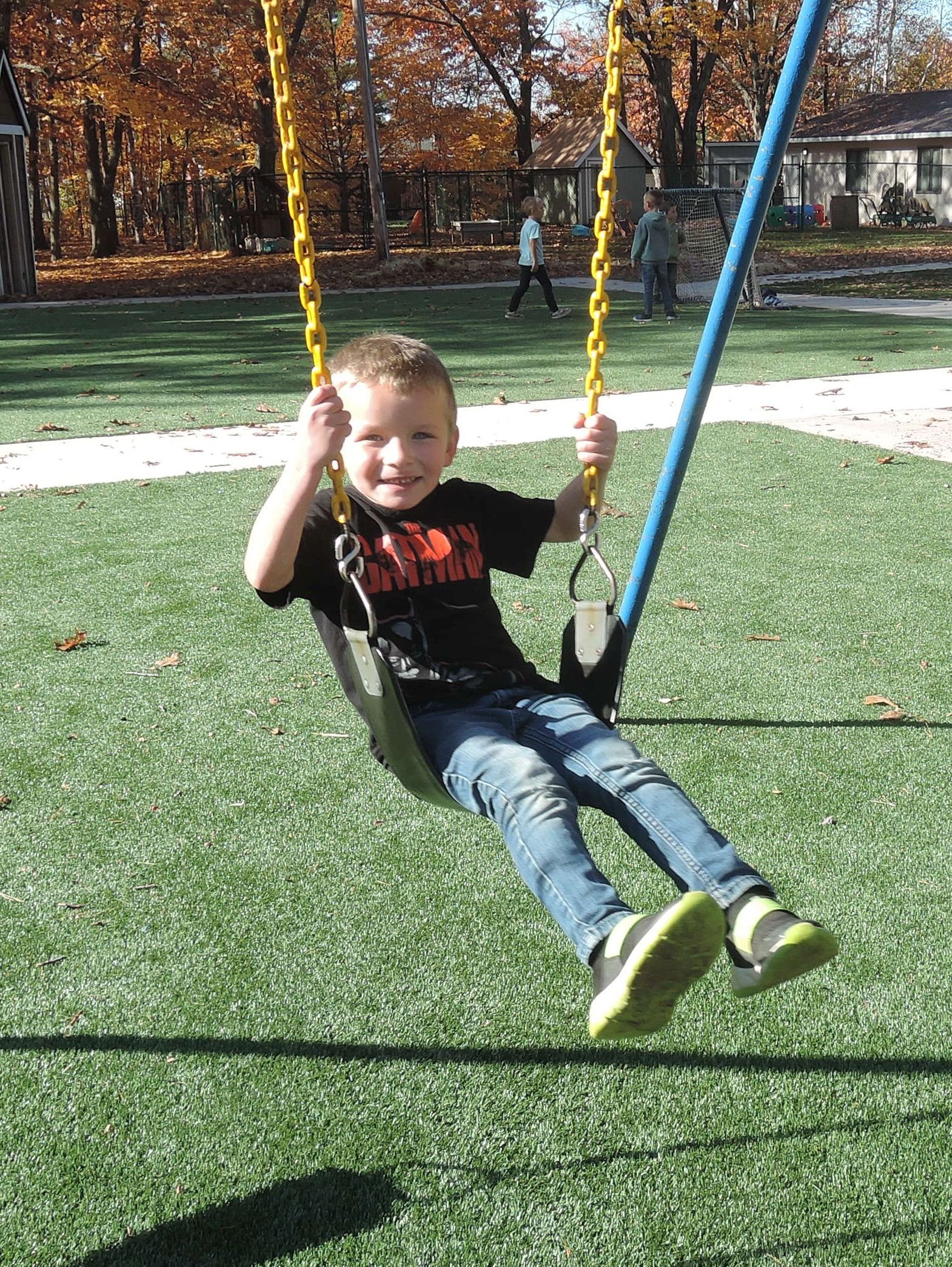 A smiling kindergarten student in mid swing during recess on a beautiful, warm, mid fall day.