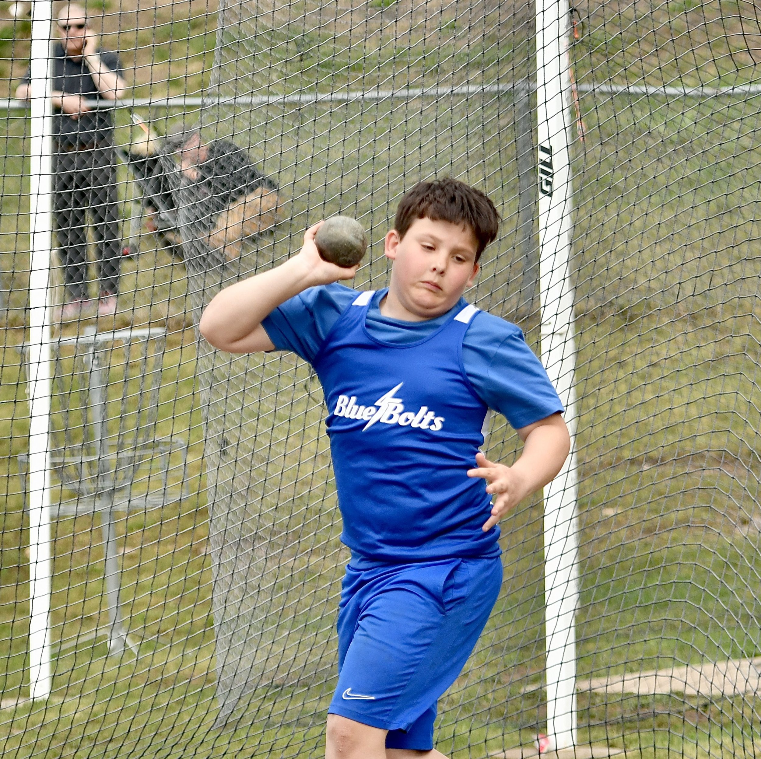 A junior high boy twisting his torso with a shot put at his ear as he begins to step into his throw.