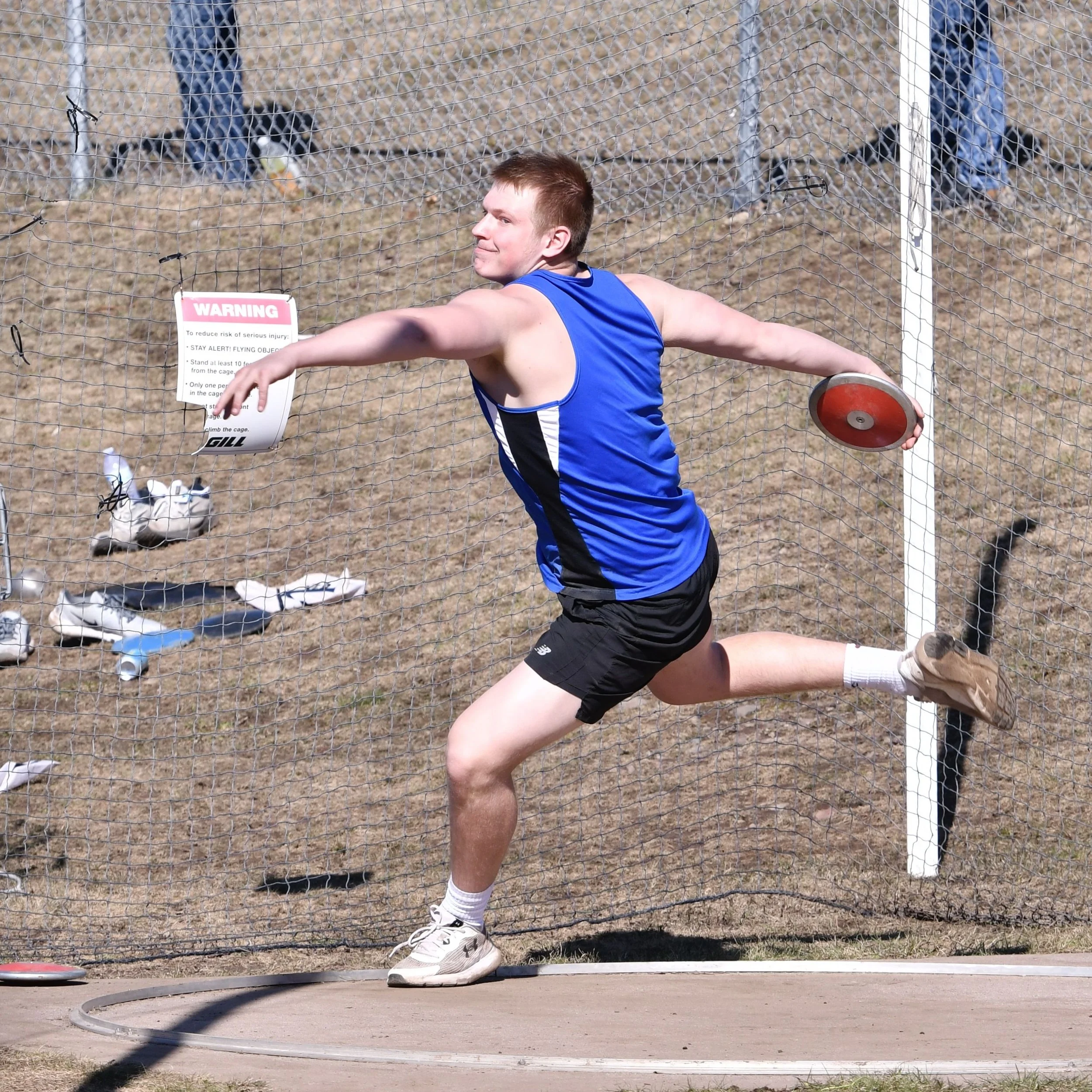 A high school male discuss thrower in mid spin with both arms fully extended prior to his final step and release.