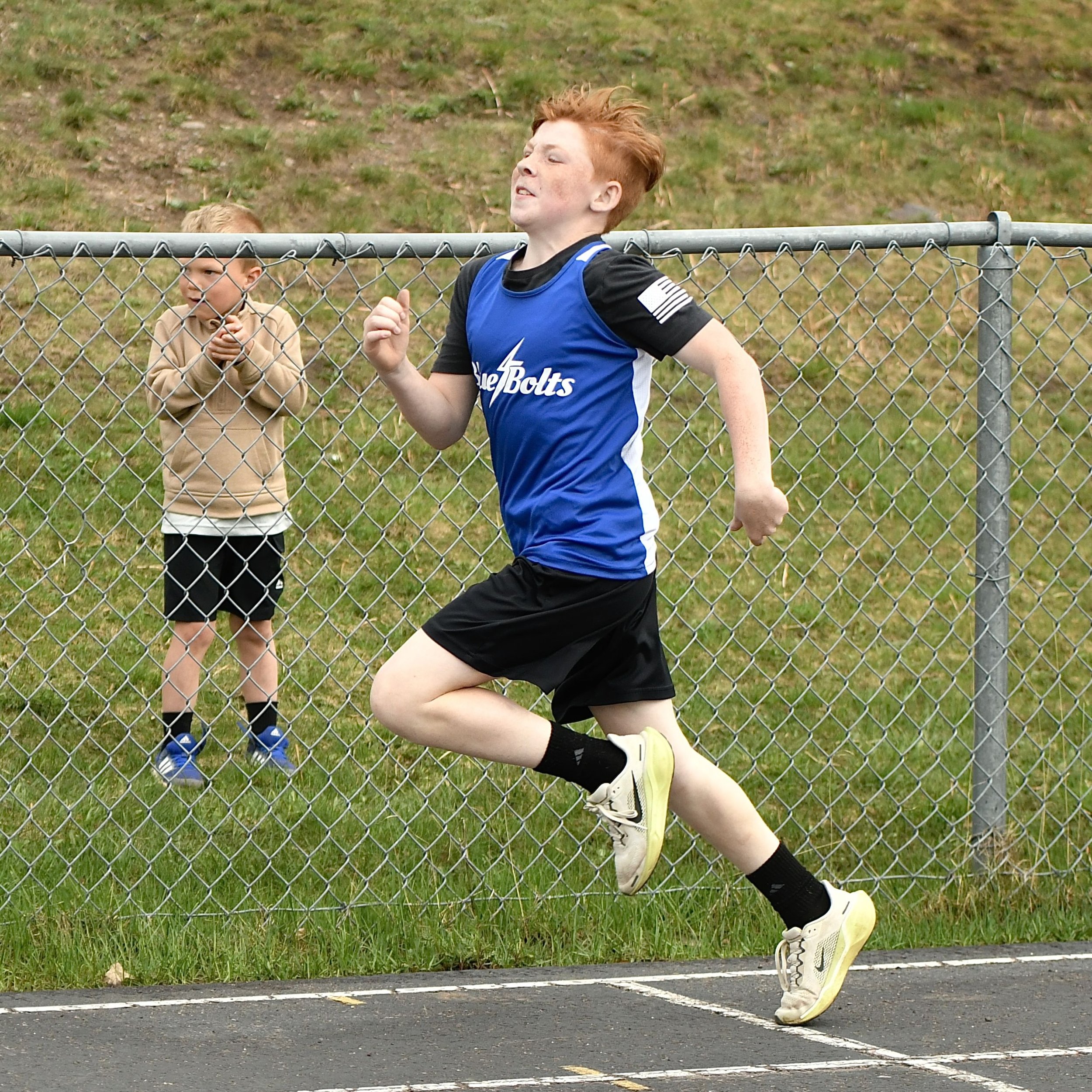A junior high boy sprinting in a race, with arms pumping aggressively and  one leg lifted high.