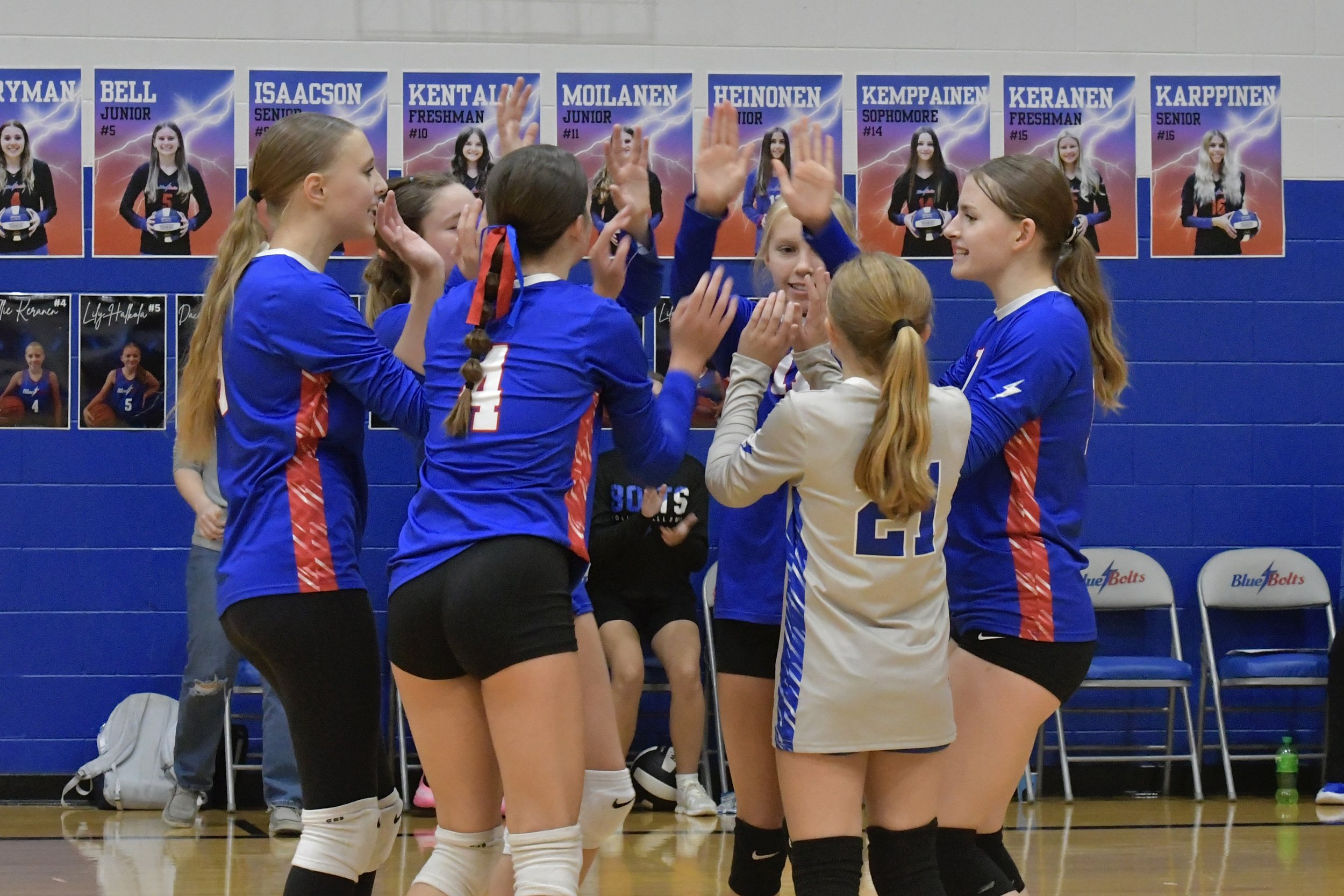 Junior varsity volleyball players circled on the court cheering and congratulating one another on a winning point.
