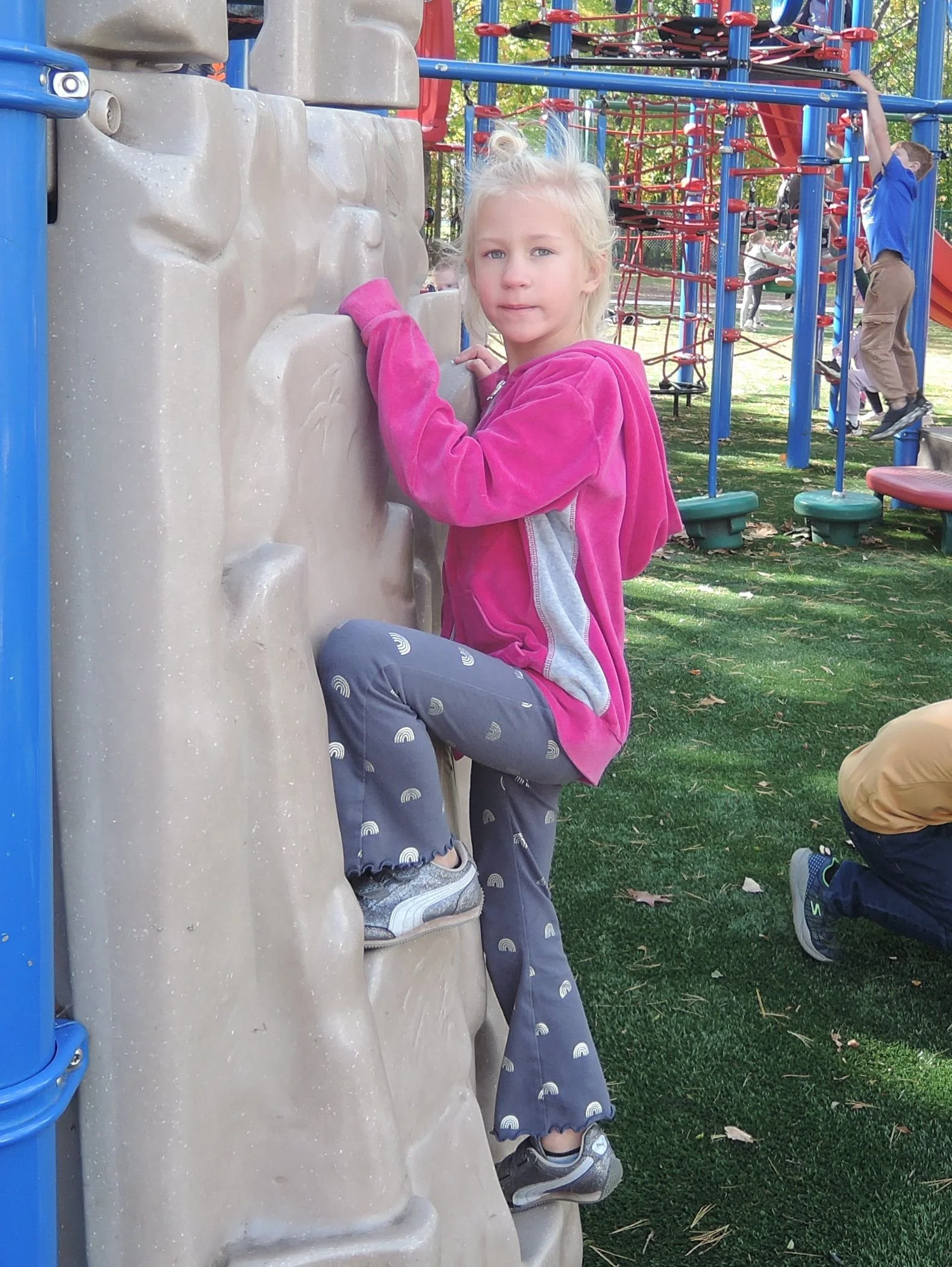 A kindergarten student half way up the climbing wall, pausing to look at the camera.