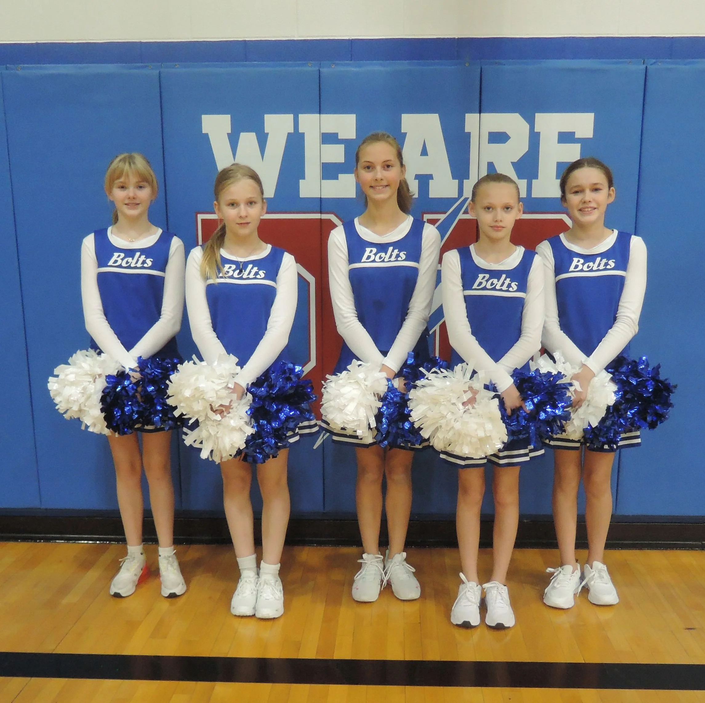 Junior high cheerleader team picture.  Five cheerleaders in a line, arms crossed at the hips holding blue and white pom-poms.