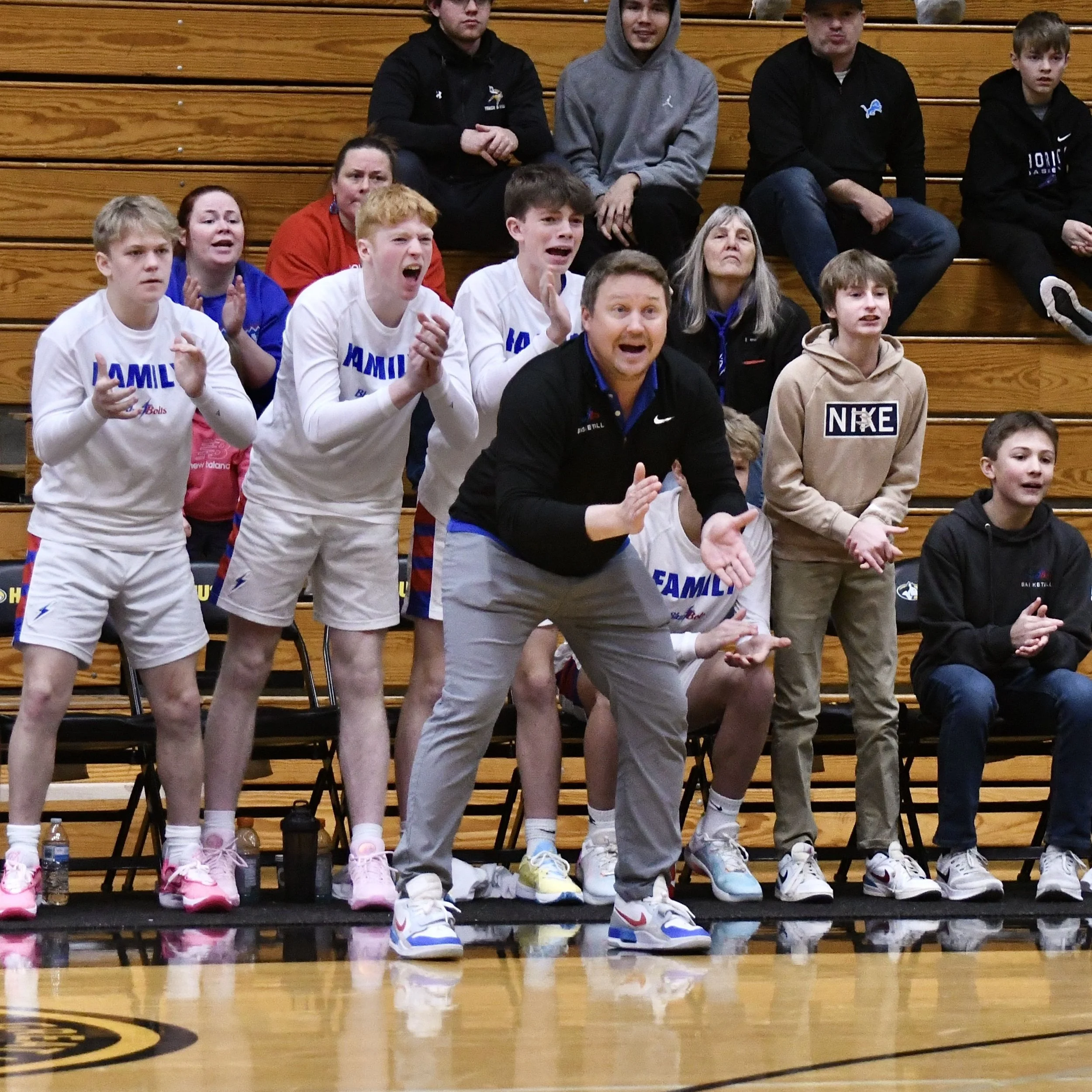 Varsity coach and team members rising off the bench enthusiastically, to cheer on a basketball play.