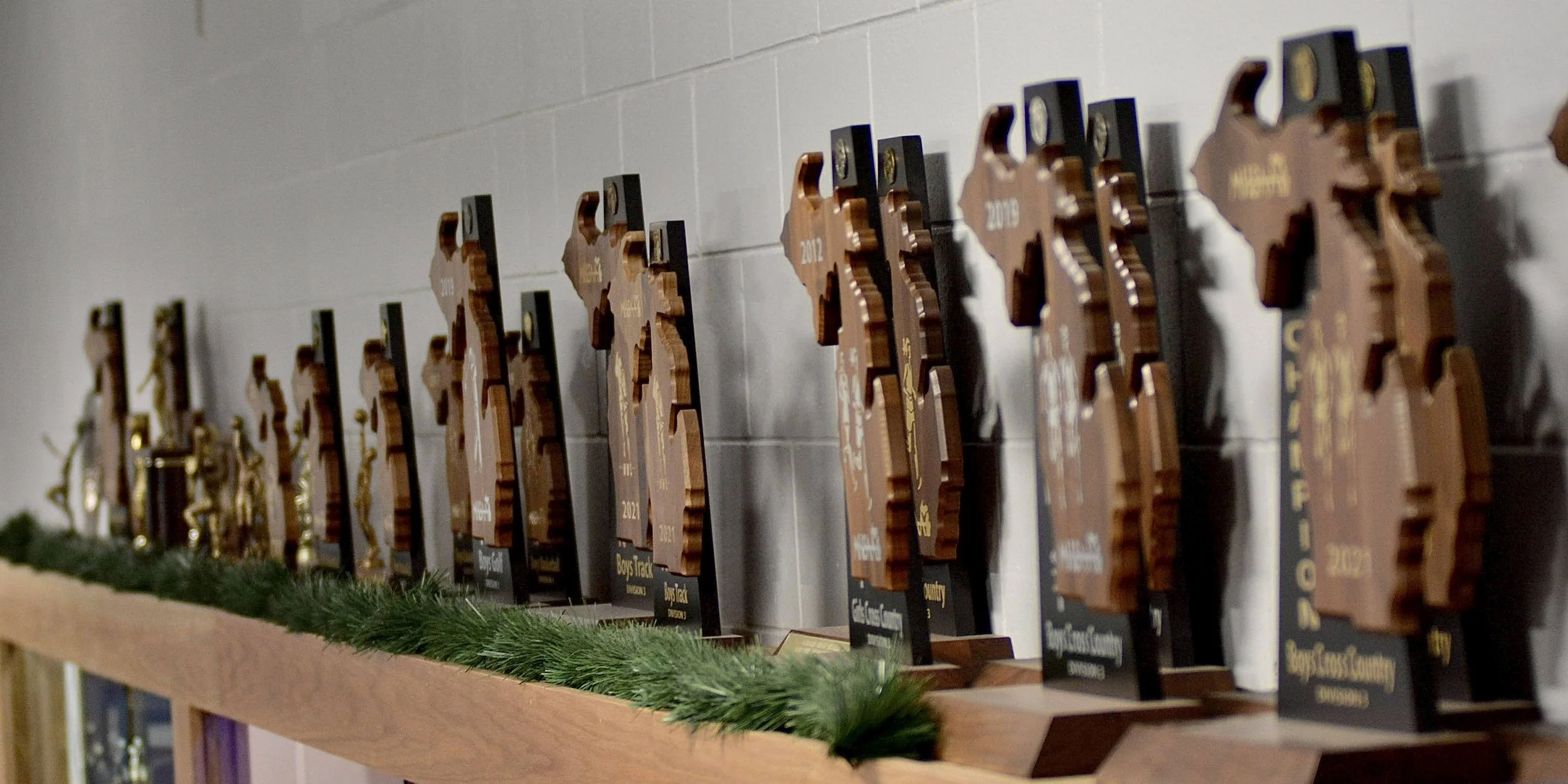 Row of MHSAA trophies on a shelf, all in the shape of upper and lower Michigan..