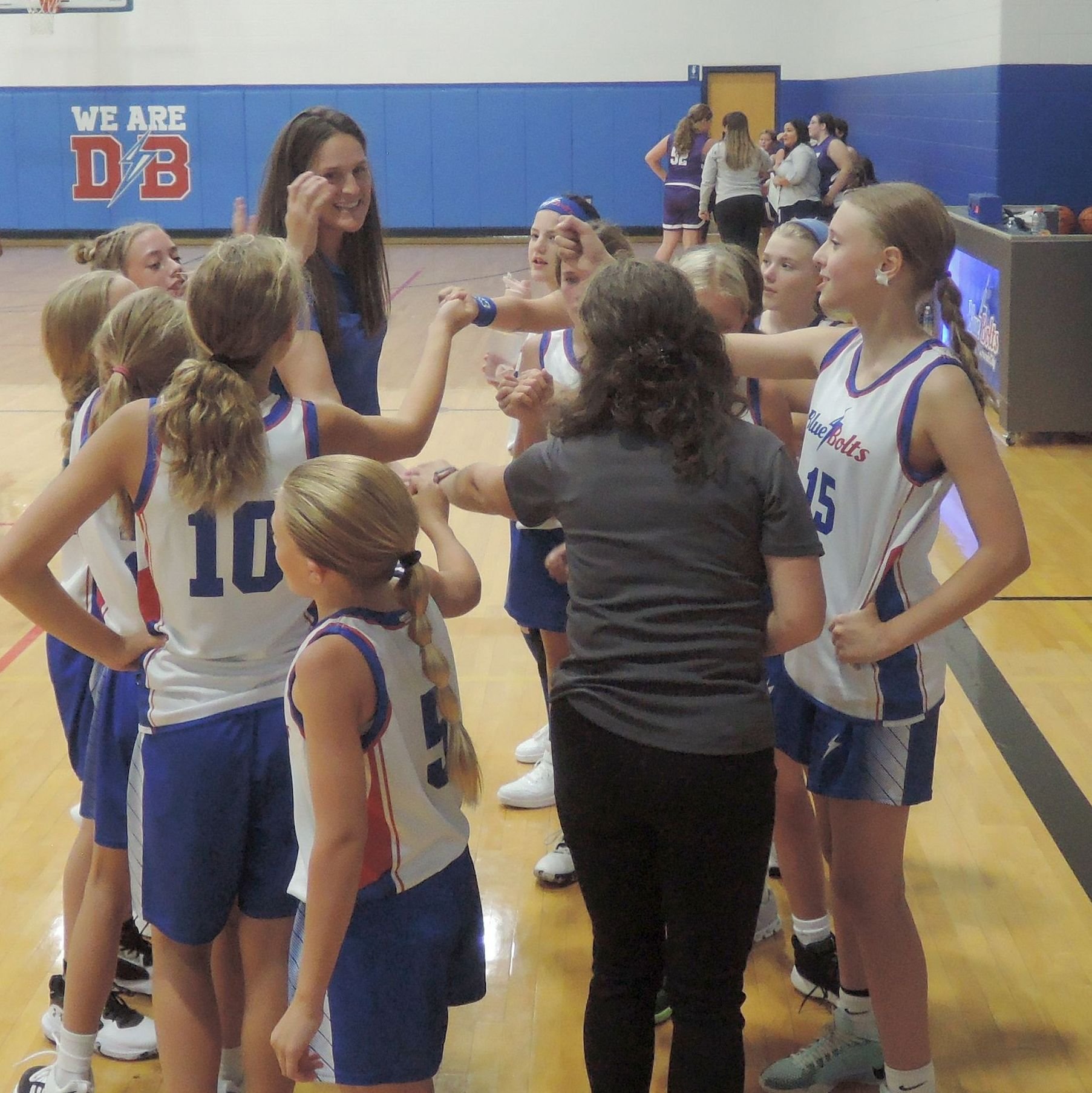 Junior high team and coach circled together at the end of a timeout with their hands joined in the center of the circle.