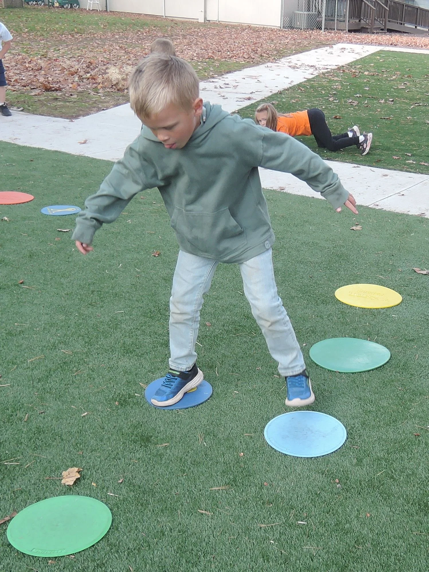 A kindergarten student, in outdoor gym class, jumping from one colorful circle to another.