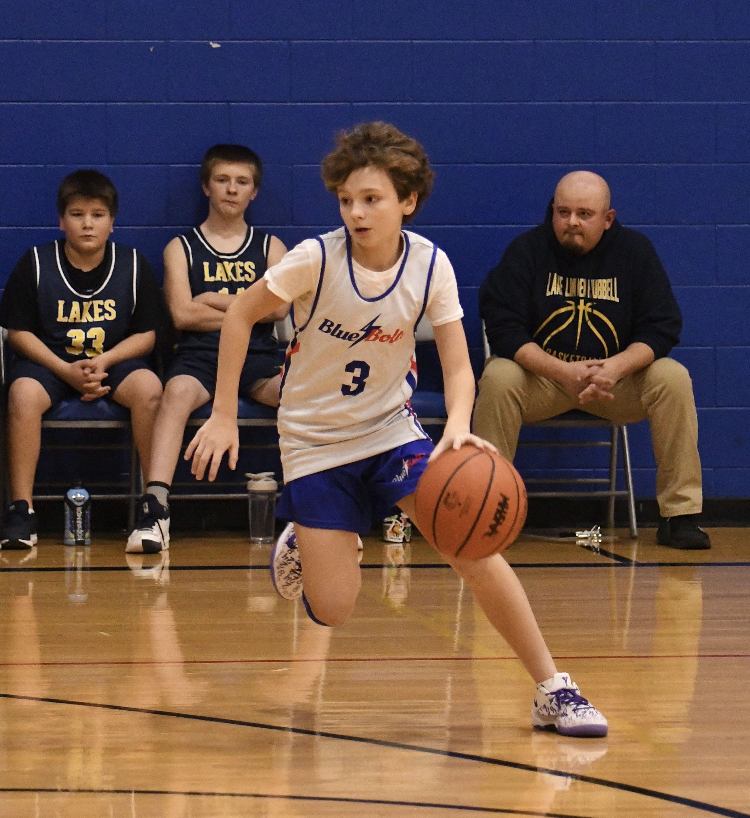 Junior high boy dribbling a basketball around the three point line.