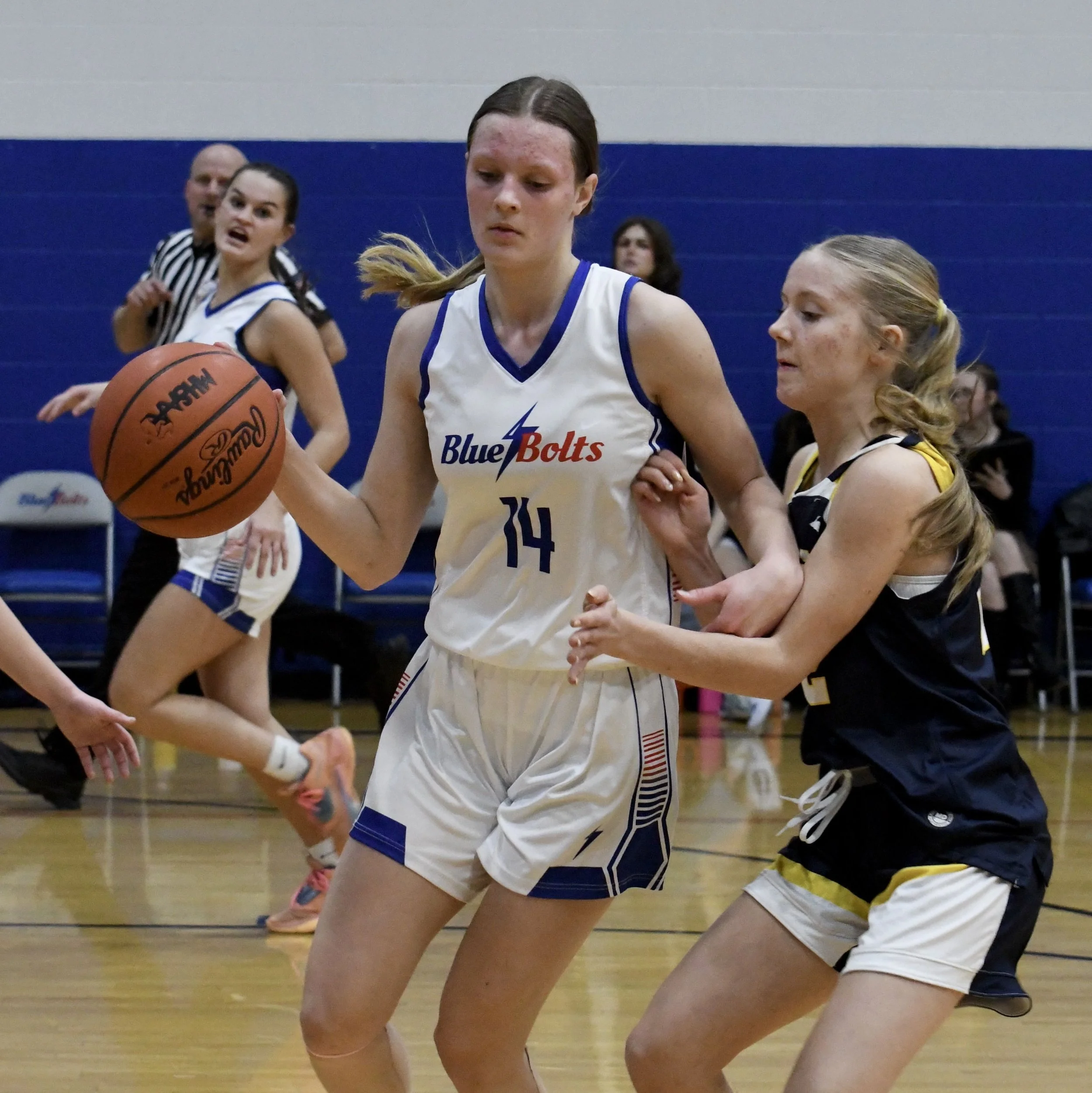 Varsity basketball female with a high dribble, being guarded closely, with teammates cutting in the background.