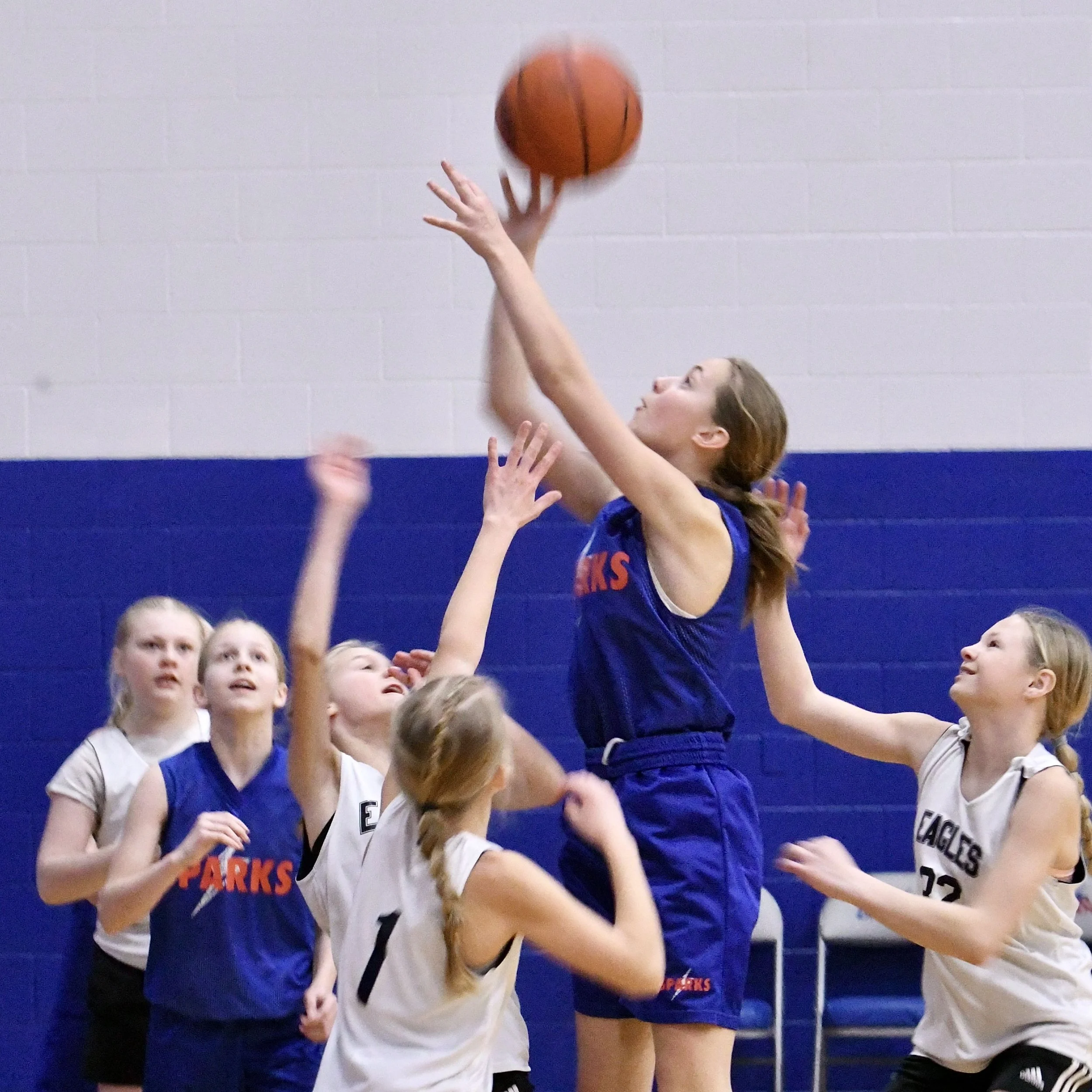 Elementary girl shooting a ball, high over a crowd of teammates and opponents.
