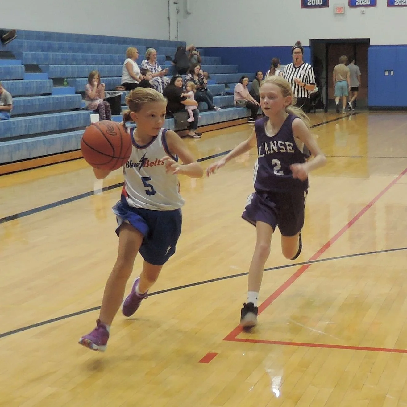 Junior high girl dribbling past her opponent, on her way to a baseline layup or shot on the left side of the court.