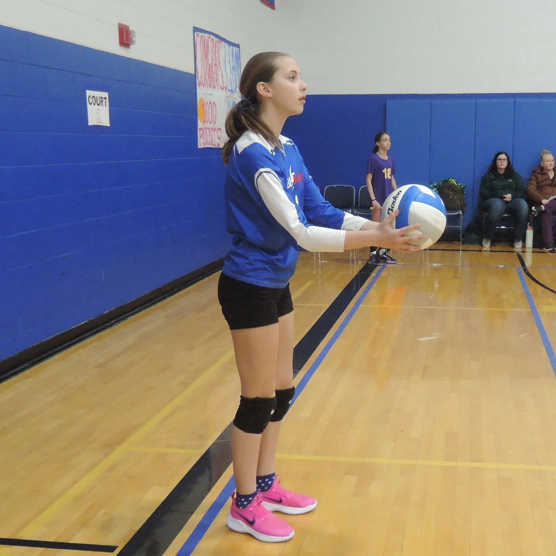 Junior high volleyball player on the back line, waiting for permission to serve, with both arms extended forward holding the ball.