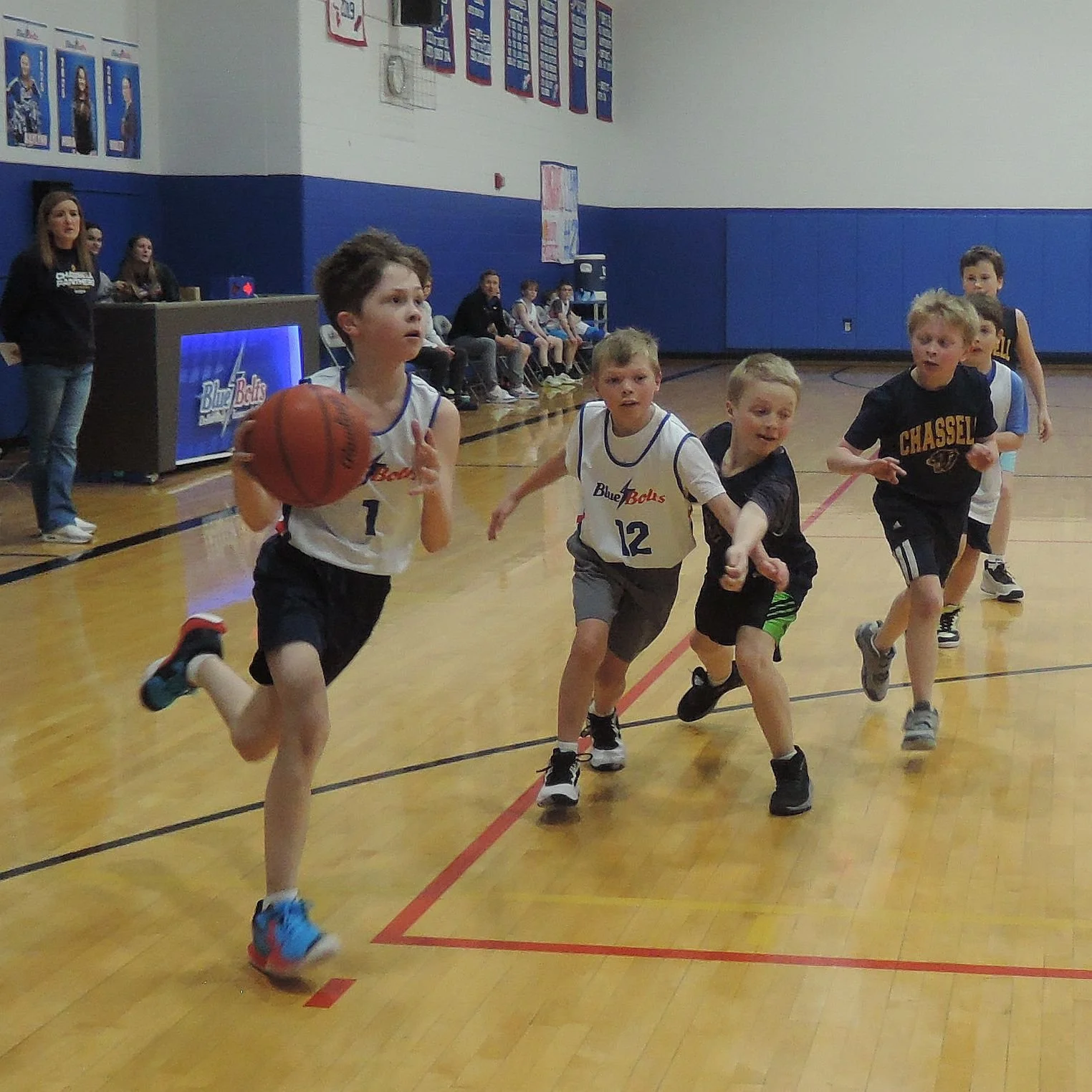 Elementary boy dribbling a basketball chased by everyone else..