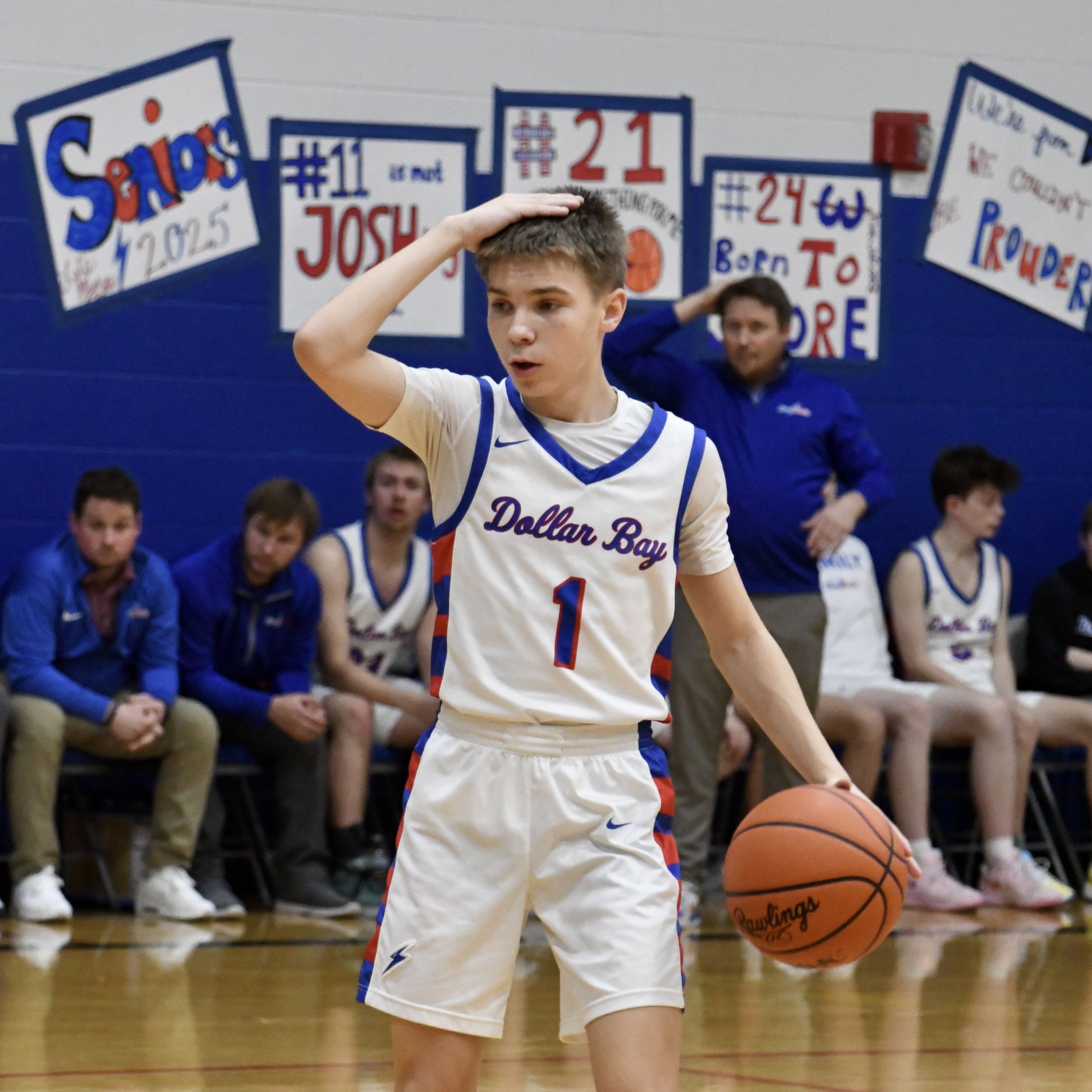 Varsity boy signaling a play at the top of the 3-point line, with his coach in the background signaling the same play.