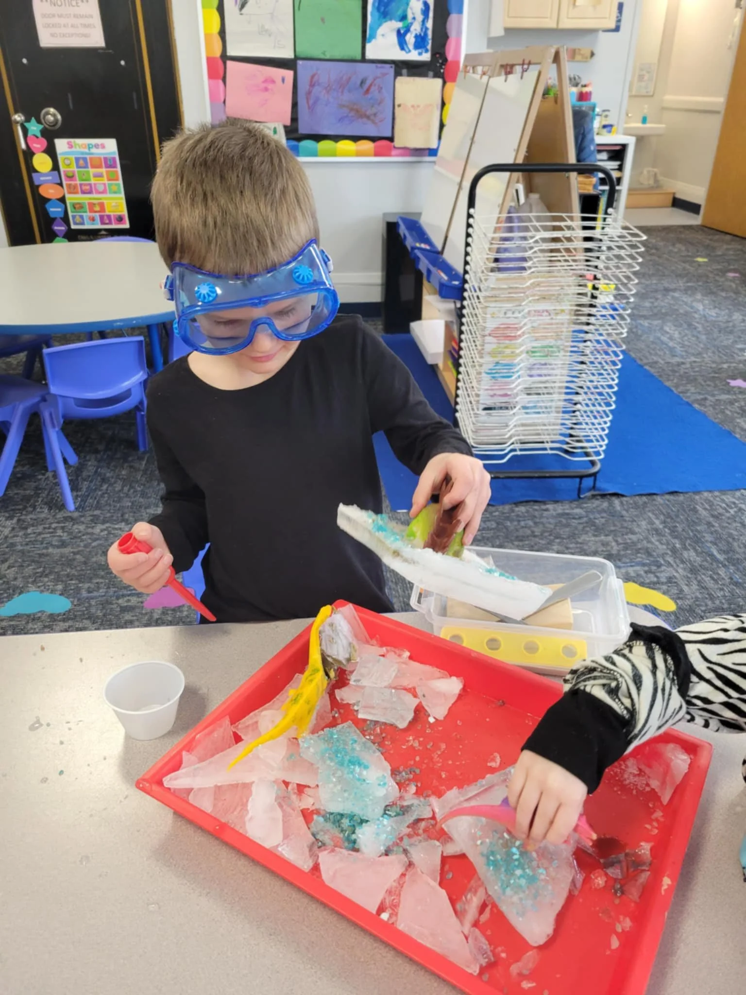 Preschool student with googles on manipulating a tray of objects in front of him.