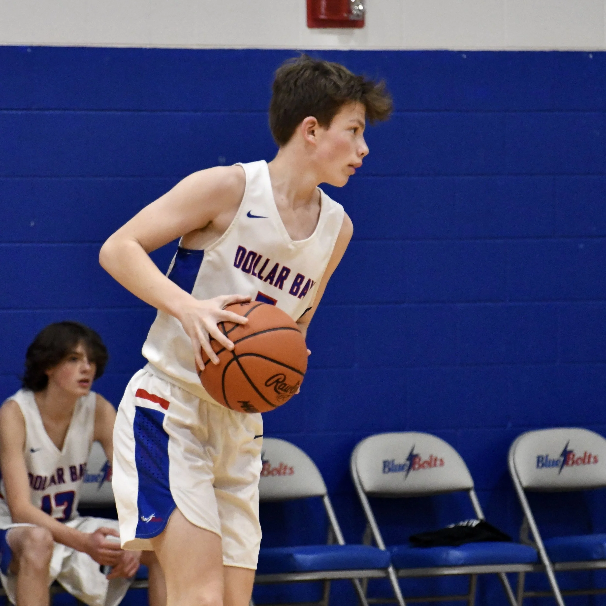 Junior varsity male holding the ball with two hands on the back hip, contemplating what to do next.