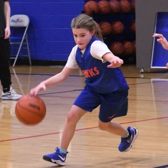 Elementary girl dribbling basketball at the top of the 3 point line.