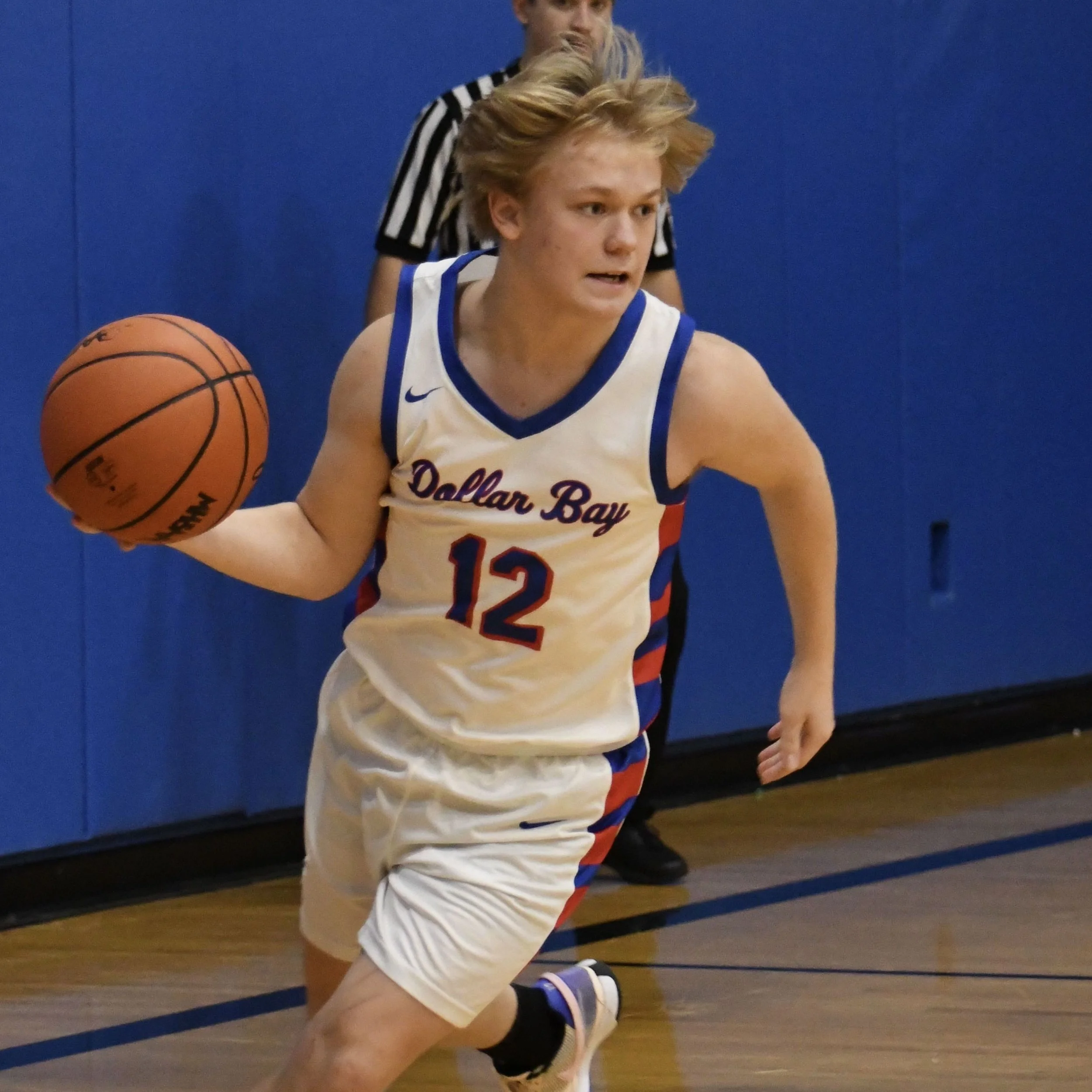 Varsity male player dribbling the ball up the court from deep in the backcourt.