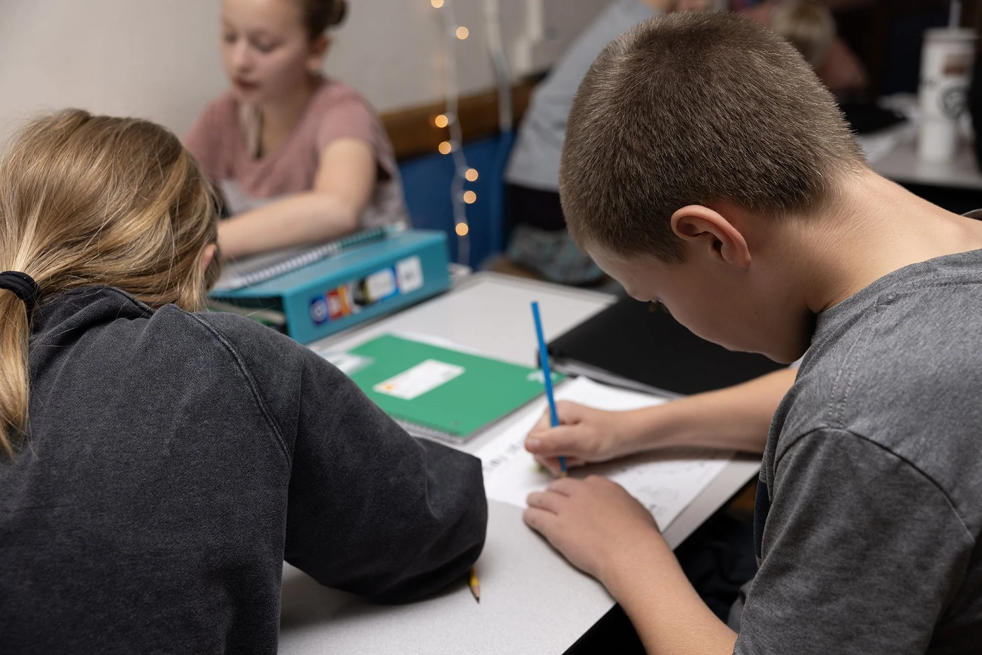 Looking over the shoulder of a student with a pencil in his hand, leaning over an assignment on his desk that he is working on.