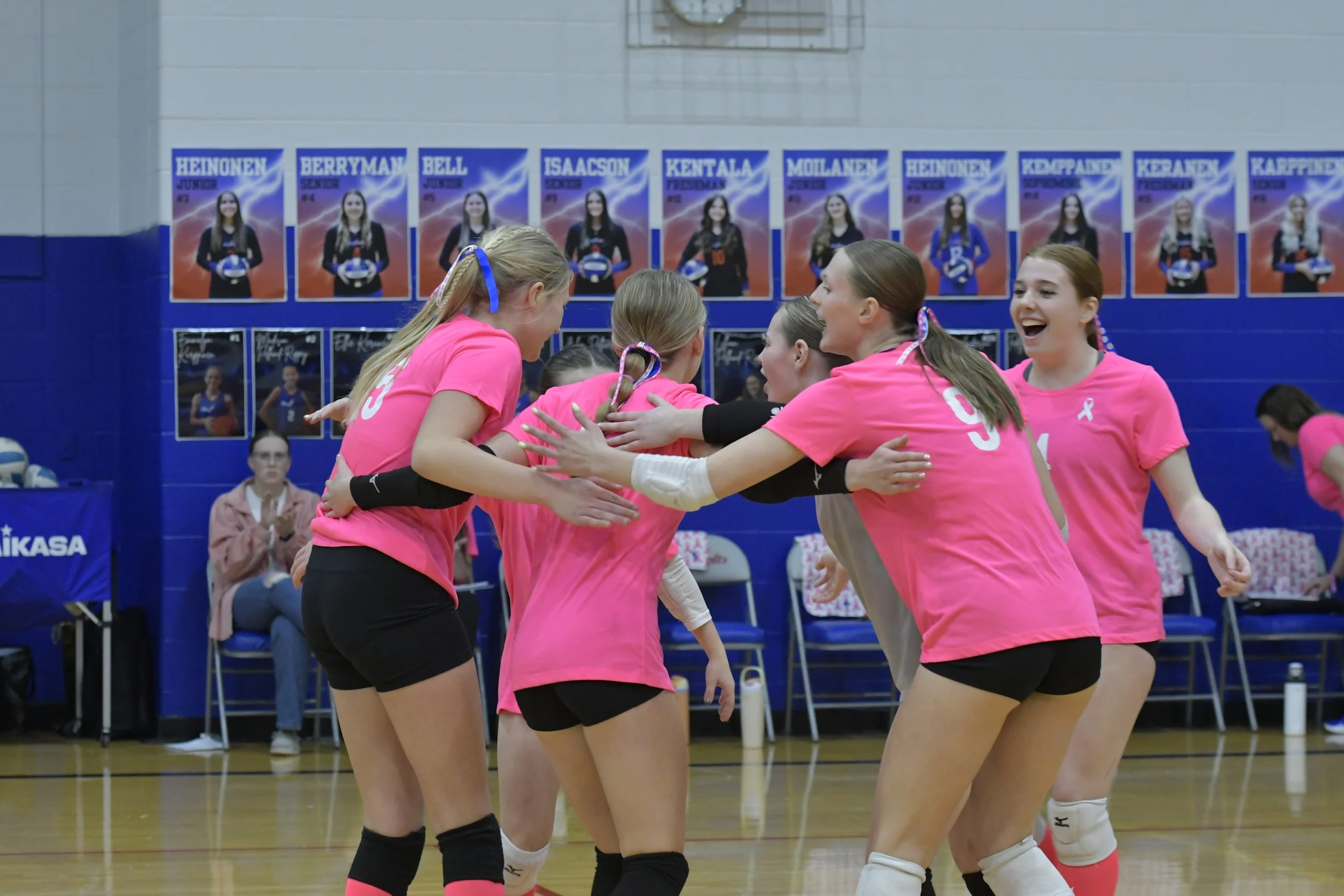 Volleyball player about to serve, with one arm raised above her head and the other hand extended and holding the the ball.