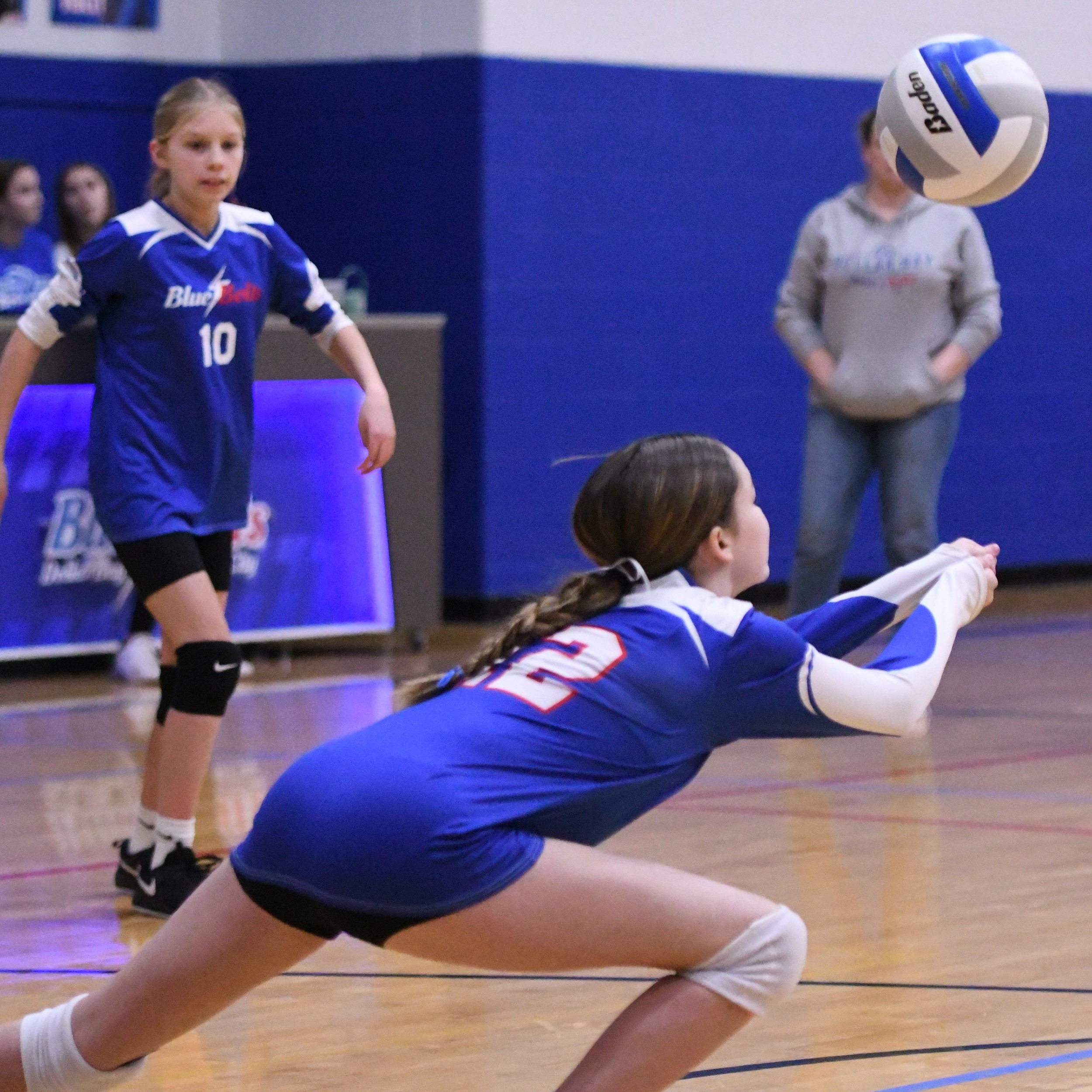 Junior high volleyball player bent over and extending forward to make a two hand bump to save the ball from hitting the court.