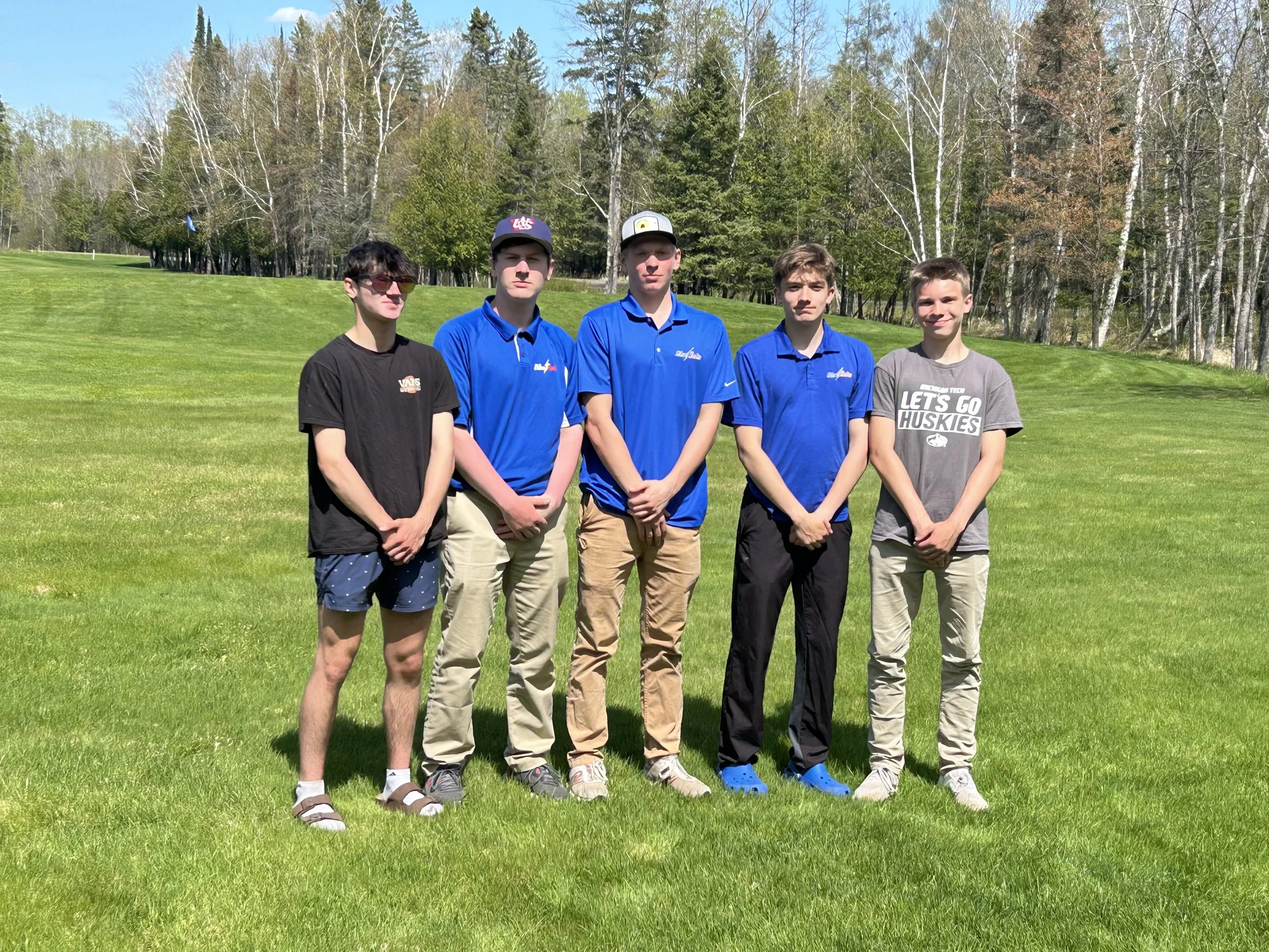 A male member of the golf team posing on the fairway with his bag of golf clubs in front of him.