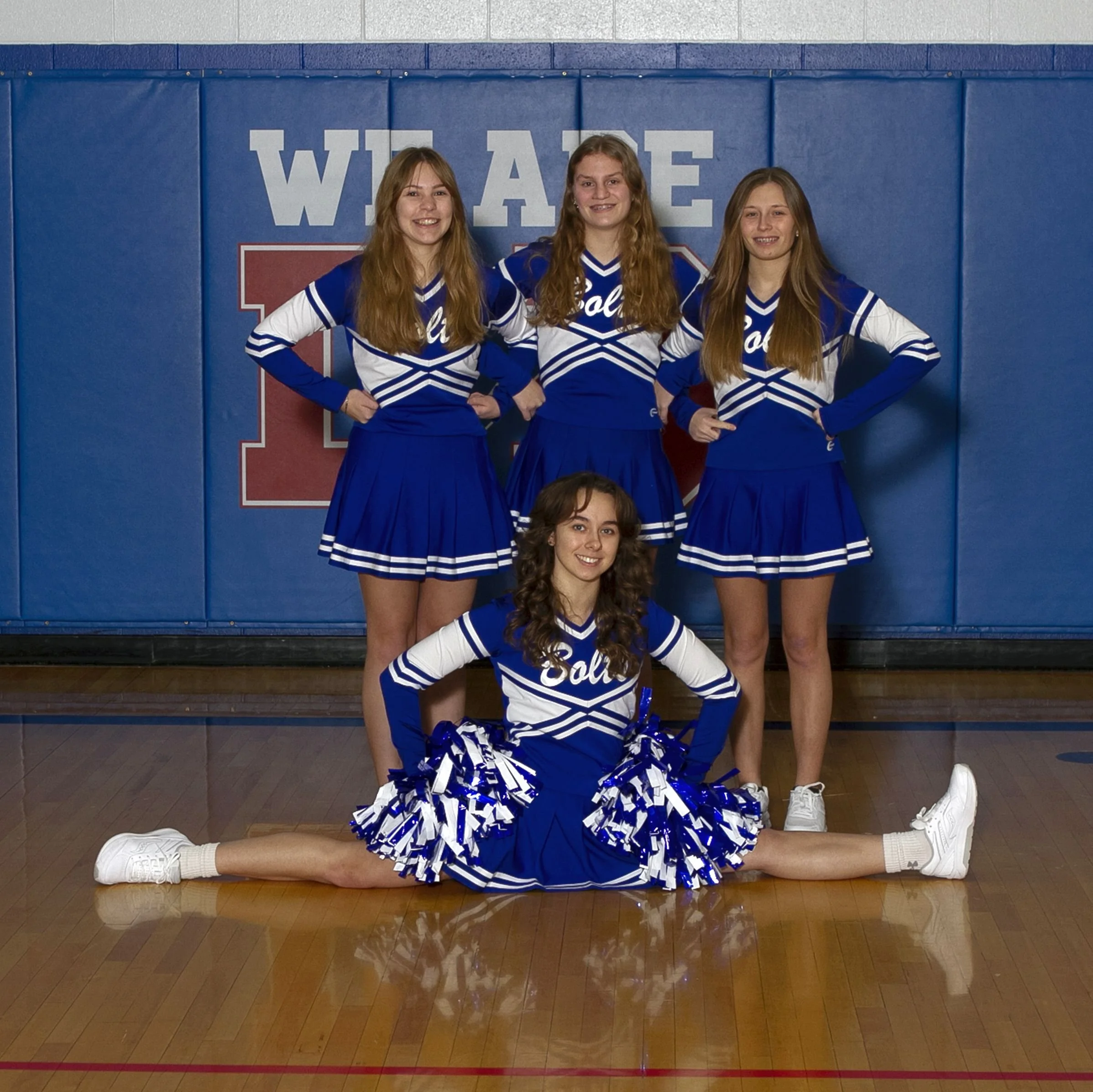 Varsity cheerleaders team picture.  Three girls standing.  One girl doing the splits on the floor in the front.