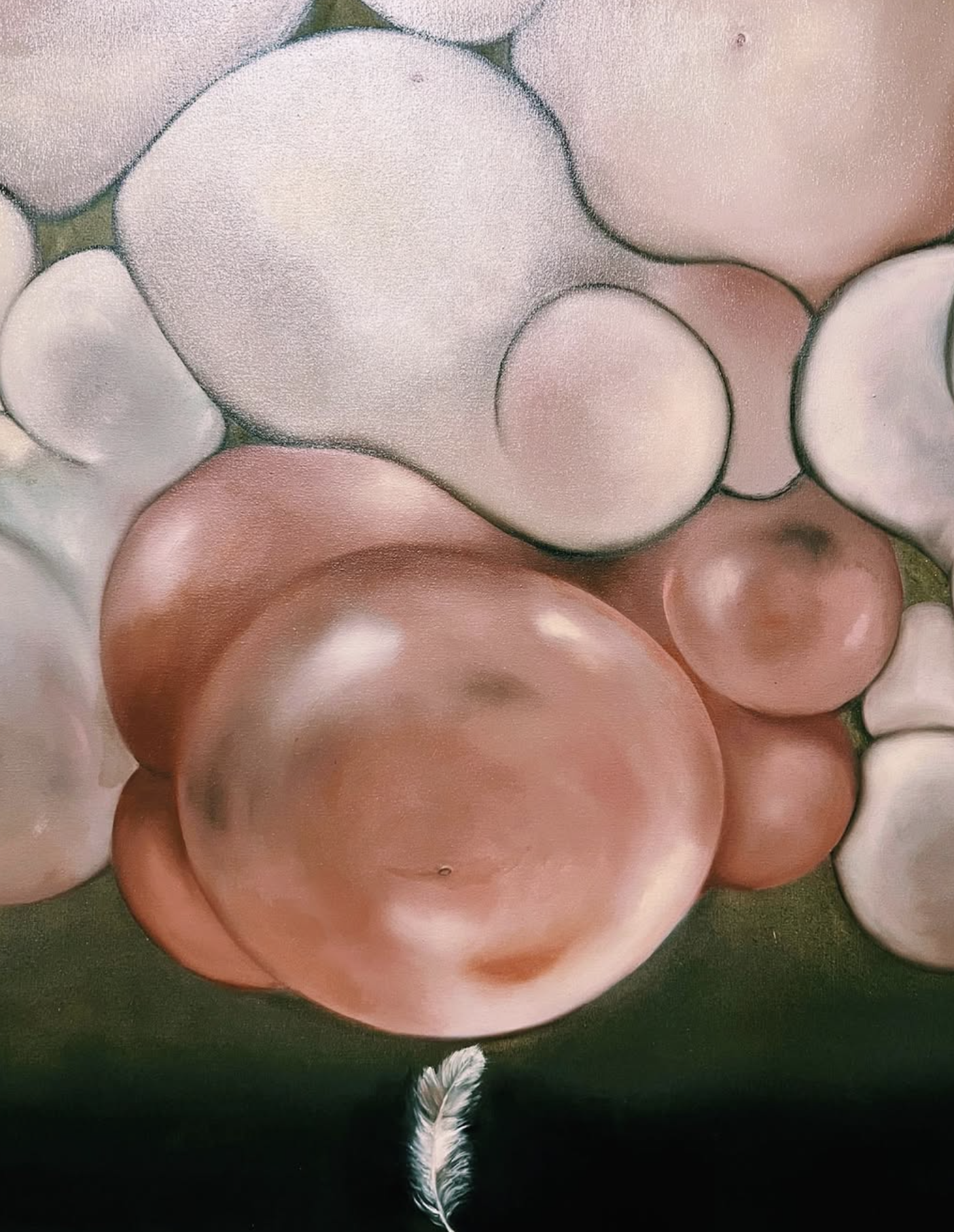 Close-up of a cluster of smooth, rounded stones with pastel shades of pink, white, and light peach, arranged on a dark green background, with a white feather at the bottom.