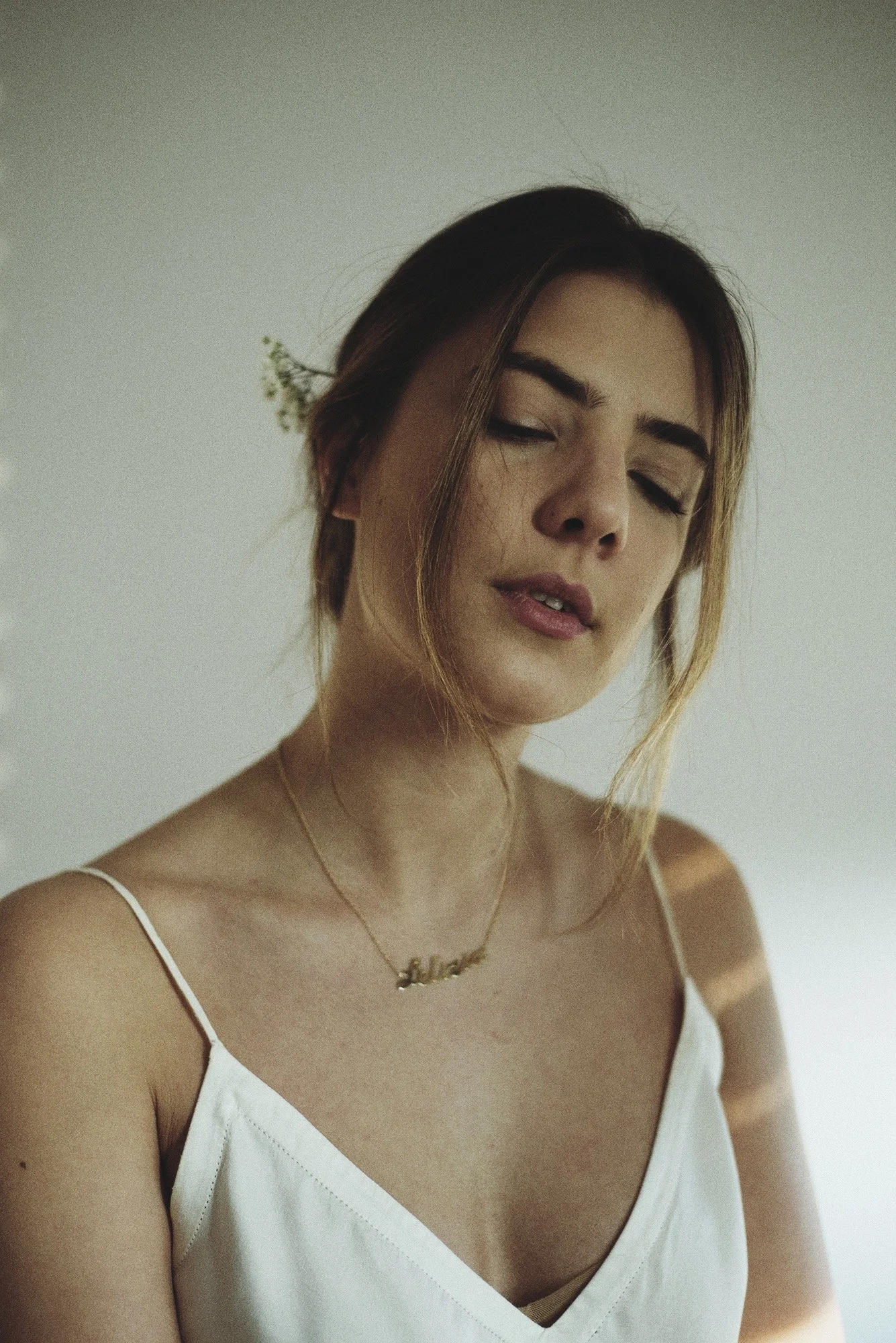 Ragazza con capelli castani e occhi chiusi, vestita con una sottoveste bianca, con una collana con il nome 'Selene' e un fiore tra i capelli.