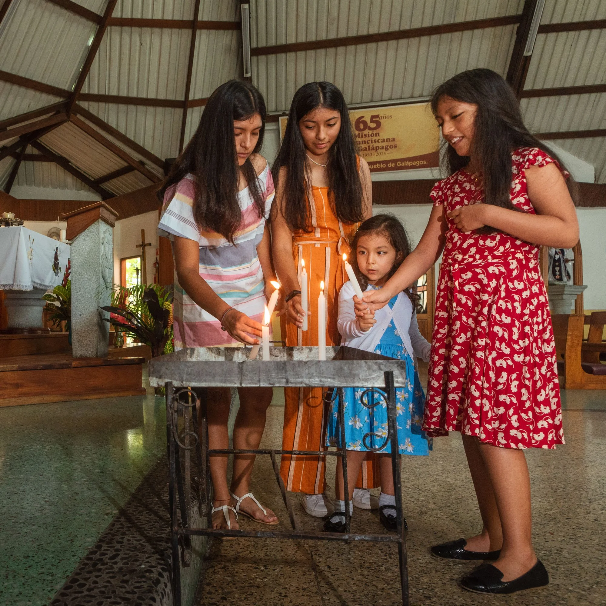 Five girls of various ages lighting candles in a church.