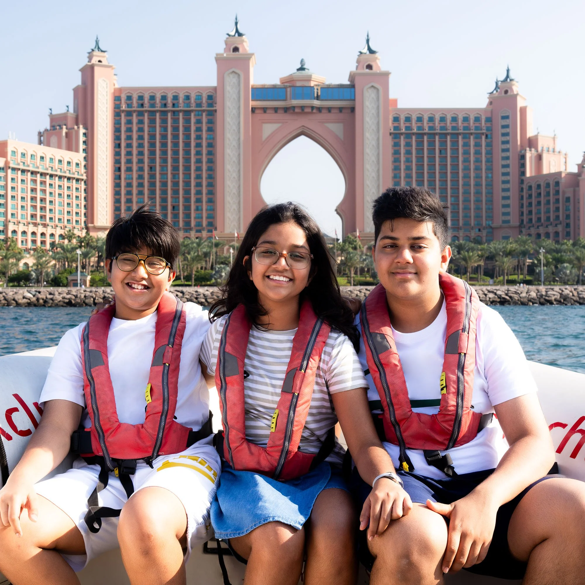 Three kids sitting on a boat with the Atlantis resort in Dubai behind them.