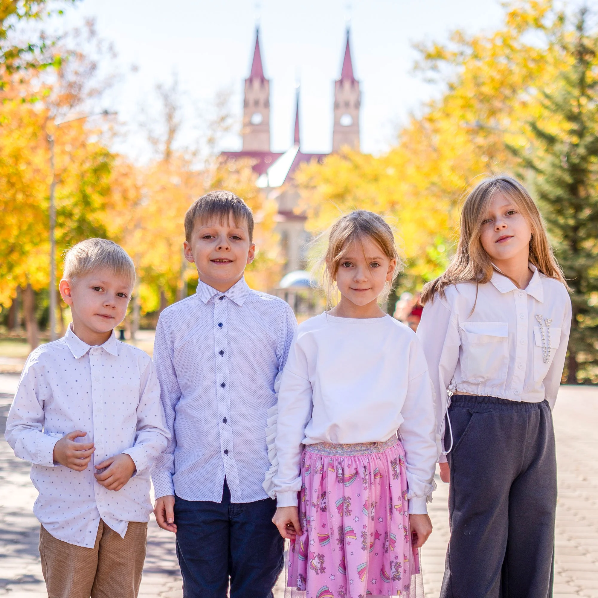 Four children standing outdoors in fall with a church in the background.