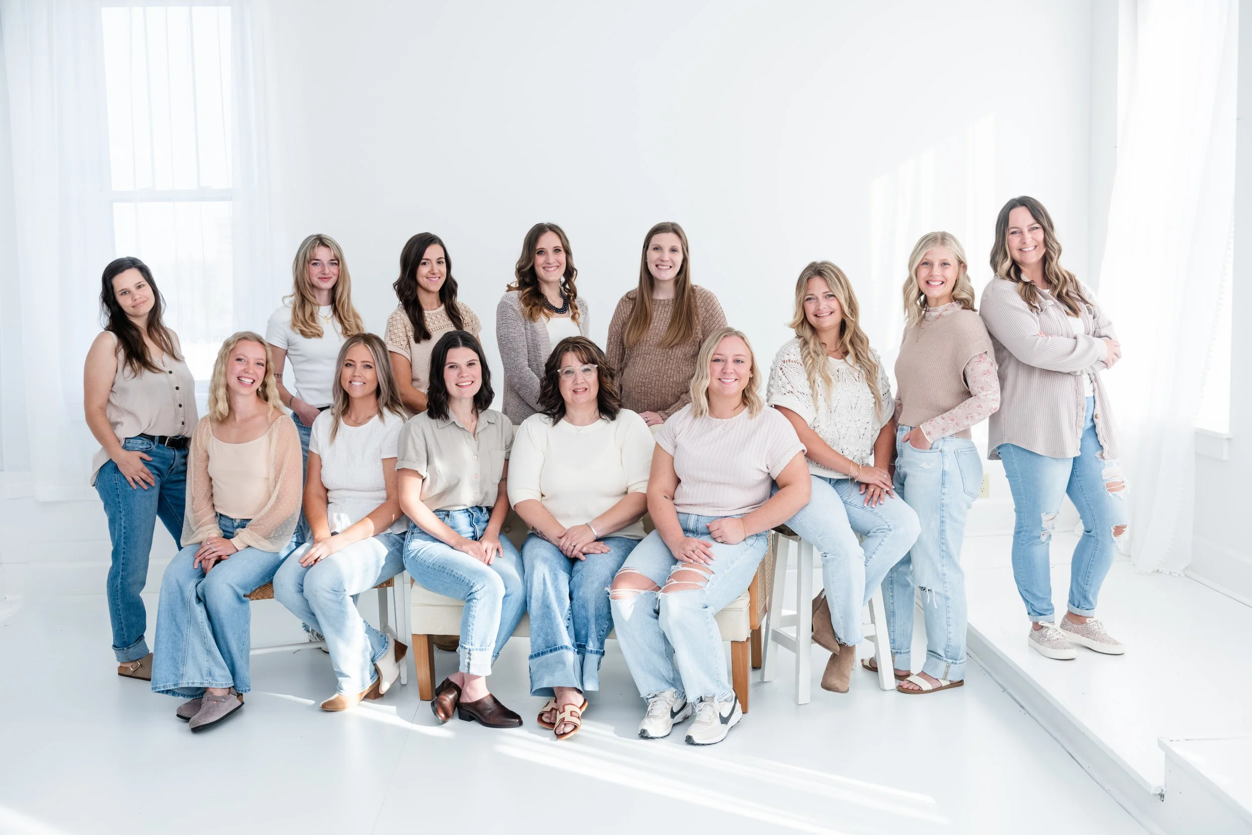 Group of 15 women posing in a bright, white room with natural light.