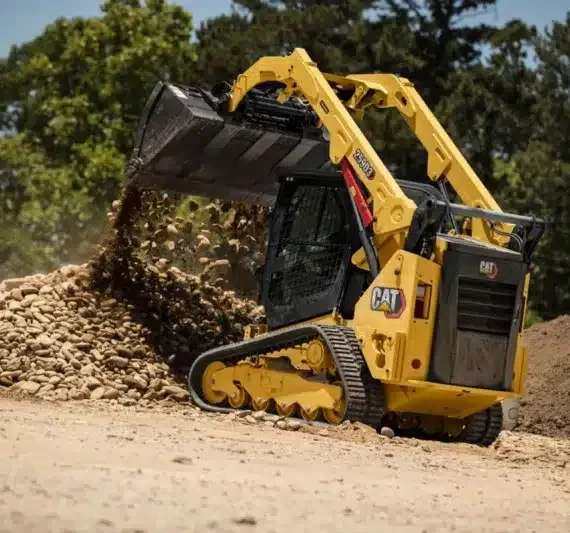 Yellow Caterpillar mini excavator with a black bucket moving dirt on a construction site at outdoors with trees in the background.