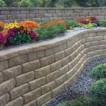 A curved stone retaining wall with colorful flowers and greenery in a garden.