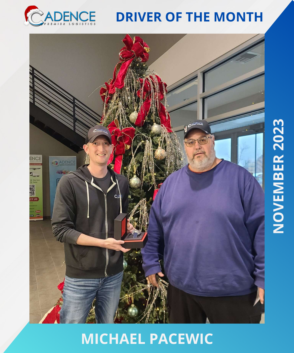 Two men standing in front of a decorated Christmas tree. One man is holding an award. They are both wearing Cadence Premier Logistics caps. There is text indicating "Driver of the Month" for November 2023 with the name Michael Pacewic.