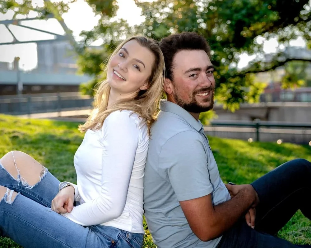 Smiling couple sitting back-to-back outdoors during a bright candid portrait session