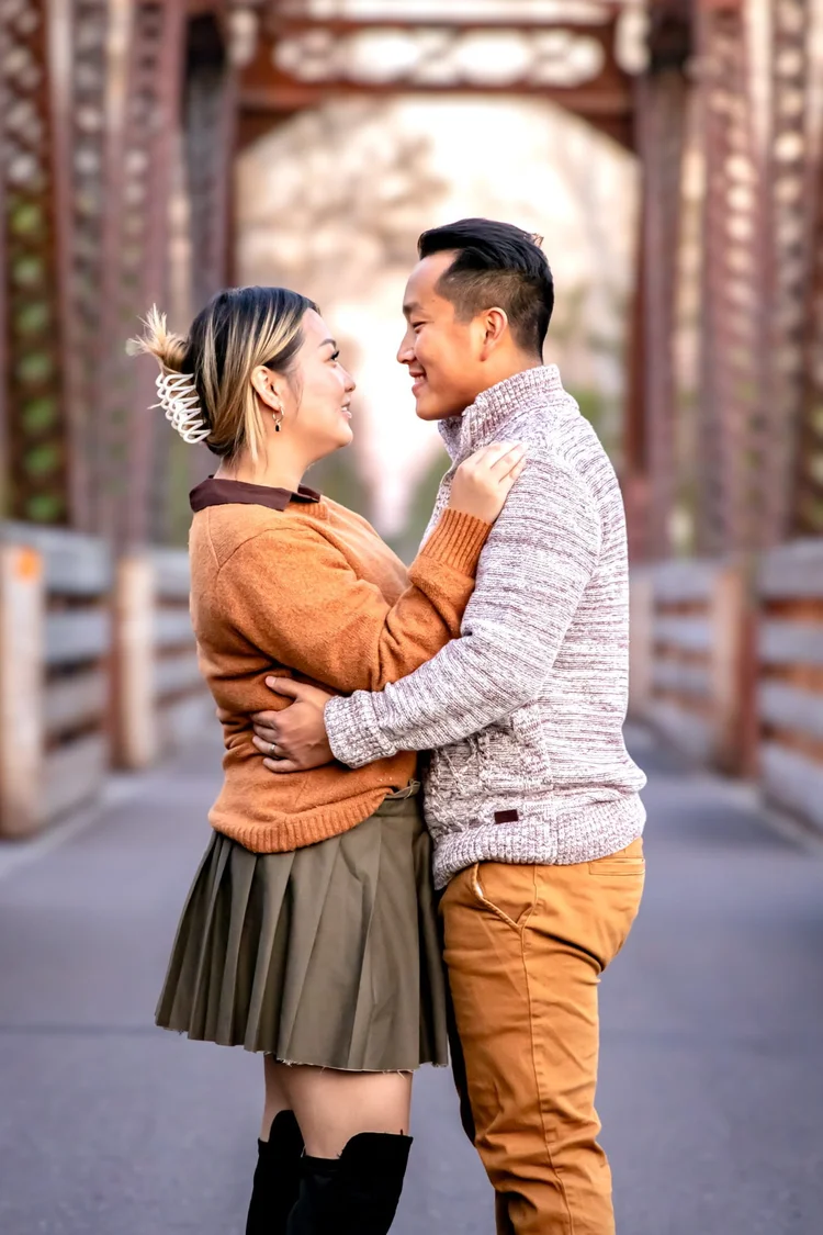 Couple smiling at each other during a close outdoor portrait on a wooden bridge