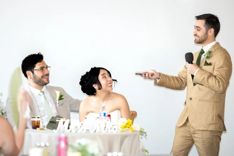 Man in a tan suit giving a reception speech as the bride and groom smile in Longmont, Colorado