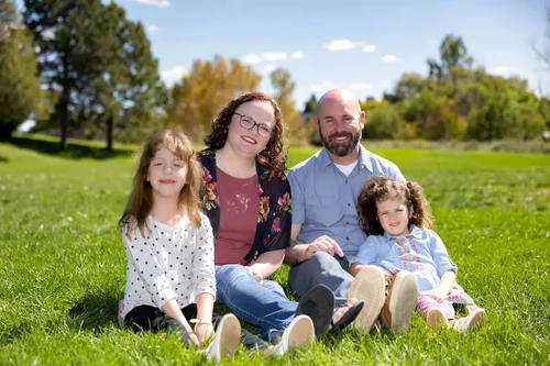 Family of four sitting together on green grass in a sunny park during an outdoor portrait session