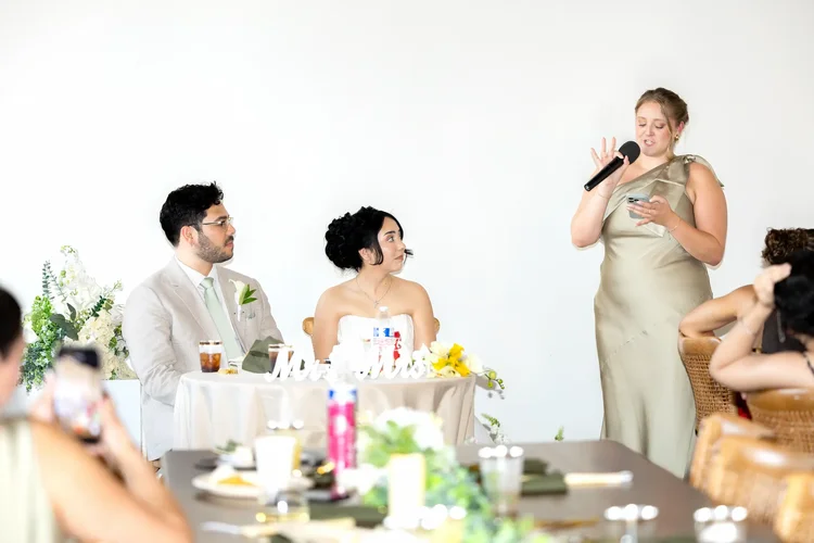 Woman in a sage green dress giving a speech beside the bride and groom at their Longmont reception
