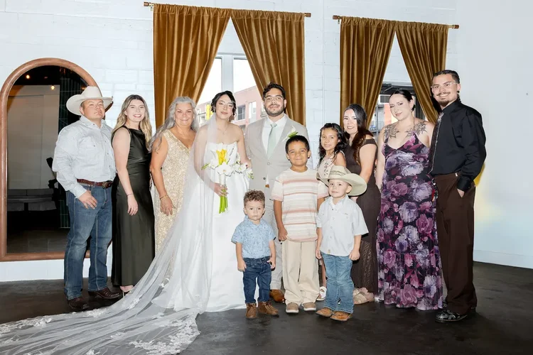 Bride and groom posing with adults and children in front of gold curtains at their Longmont wedding