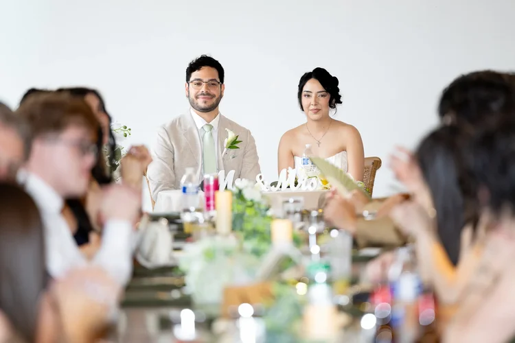 Bride and groom seated at their reception table with wedding guests in the foreground in Longmont, Colorado