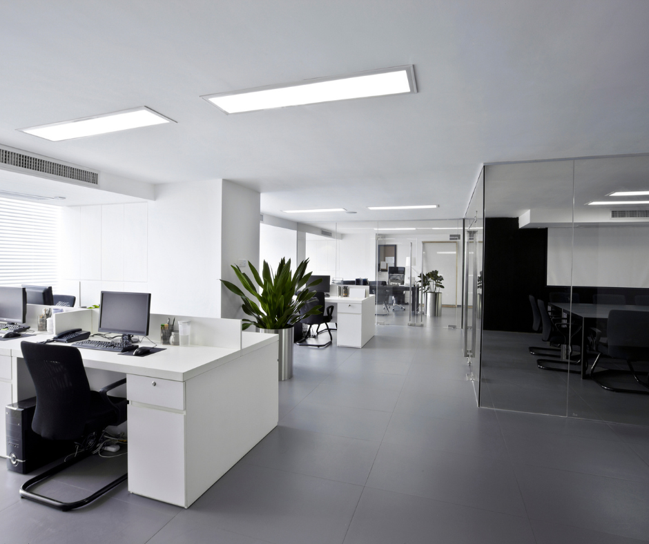 Bureau moderne avec des postes de travail blancs, plantes vertes, et parois en verre.