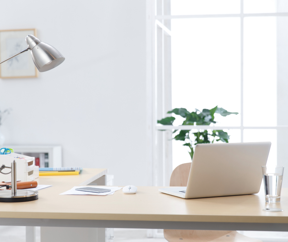Bureau moderne avec ordinateur portable, lampe de bureau, verre d'eau, plante verte, smartphone et papiers. Intérieur lumineux et épuré.