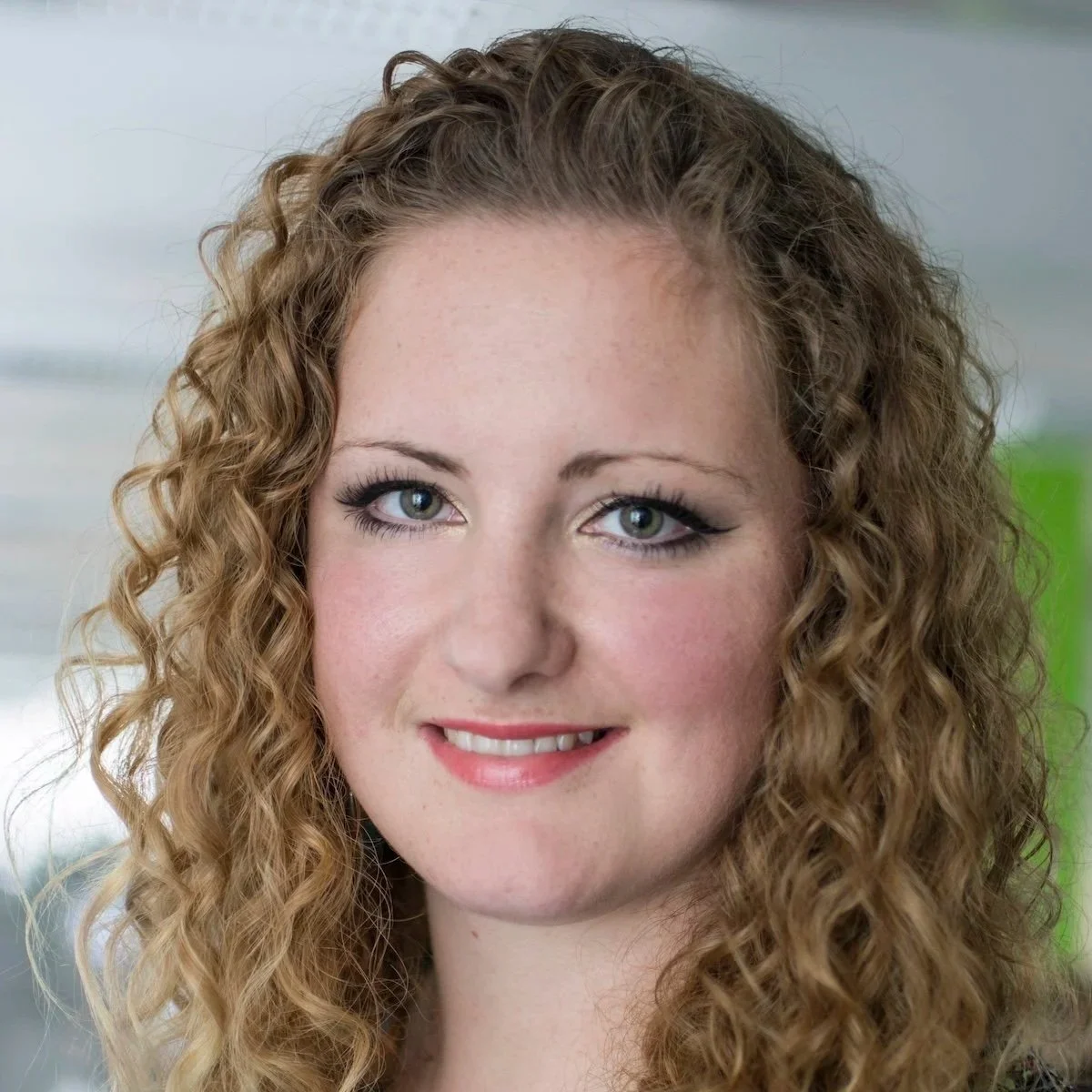 Close-up of a young woman with curly light brown hair, blue eyes, and a friendly smile.