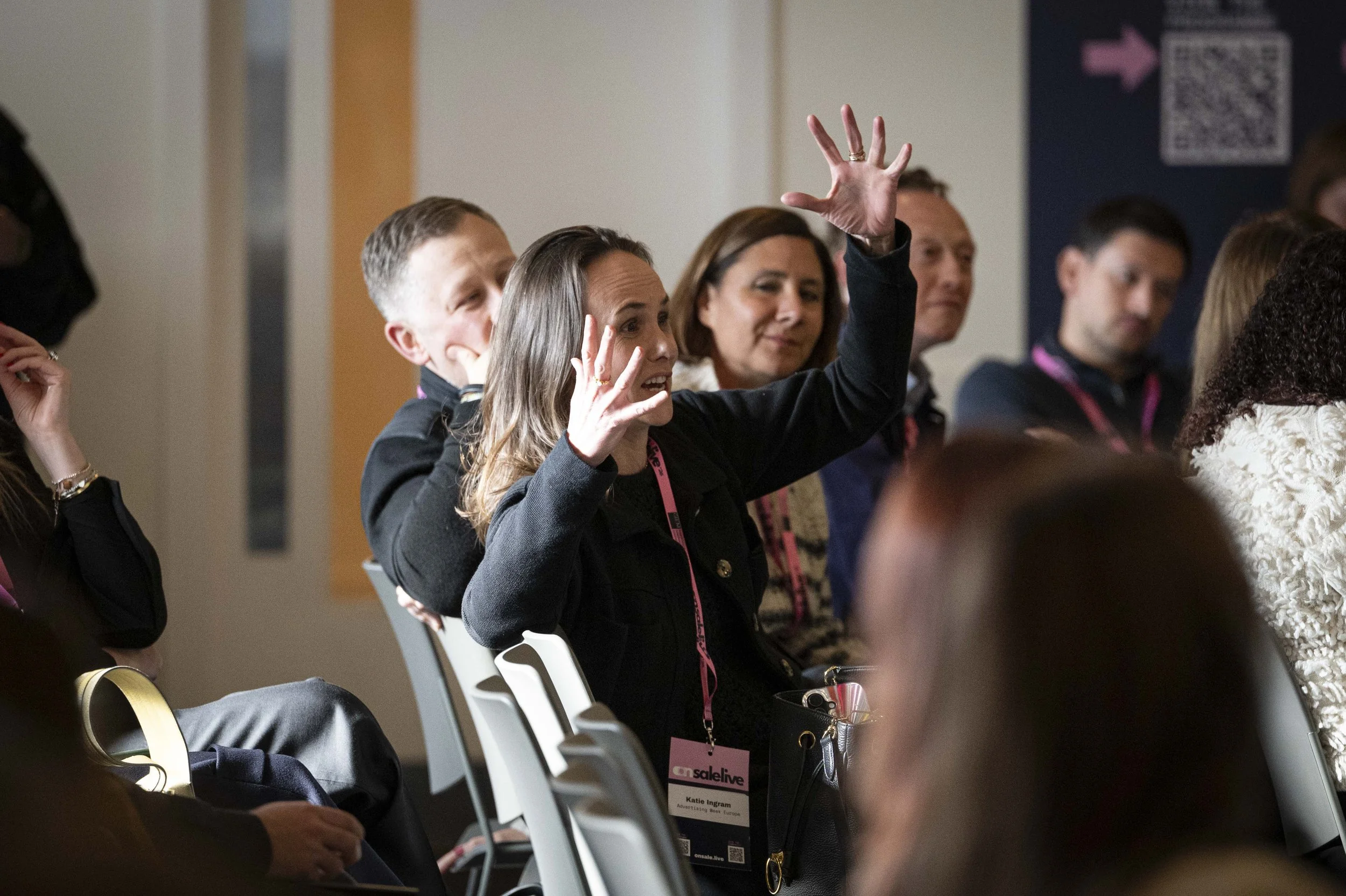 A group of people attending a conference, with one woman raising her hand to ask a question.