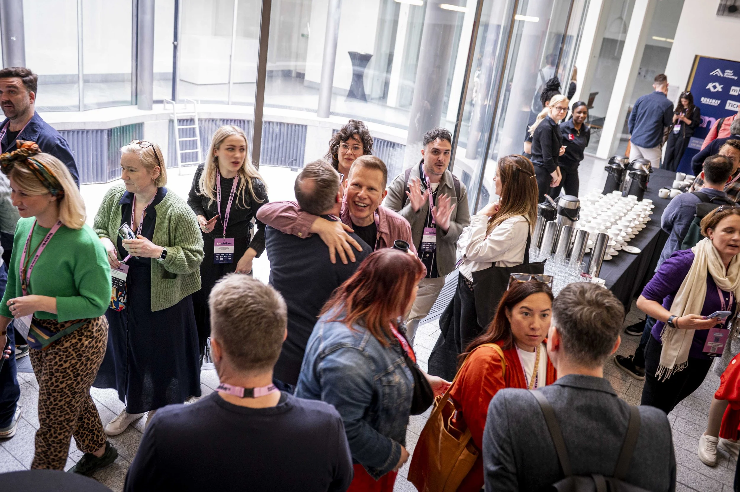 People mingling at a conference reception with a coffee table in the background, large windows, and a glass door