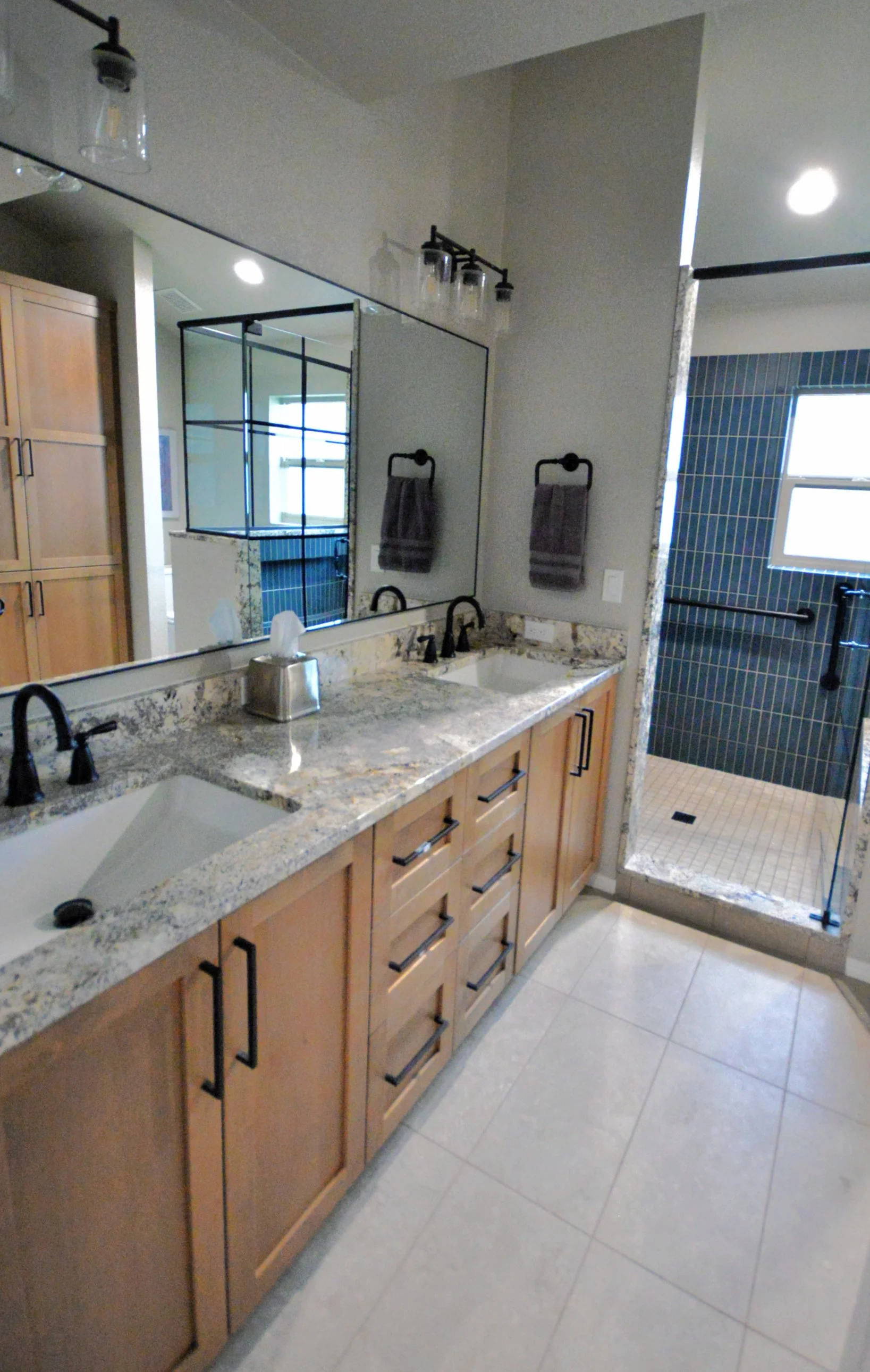 Primary bathroom with light stained wood cabinets, granite countertop and walk-in blue tiled shower with large shower seat incorporating the granite countertop material.