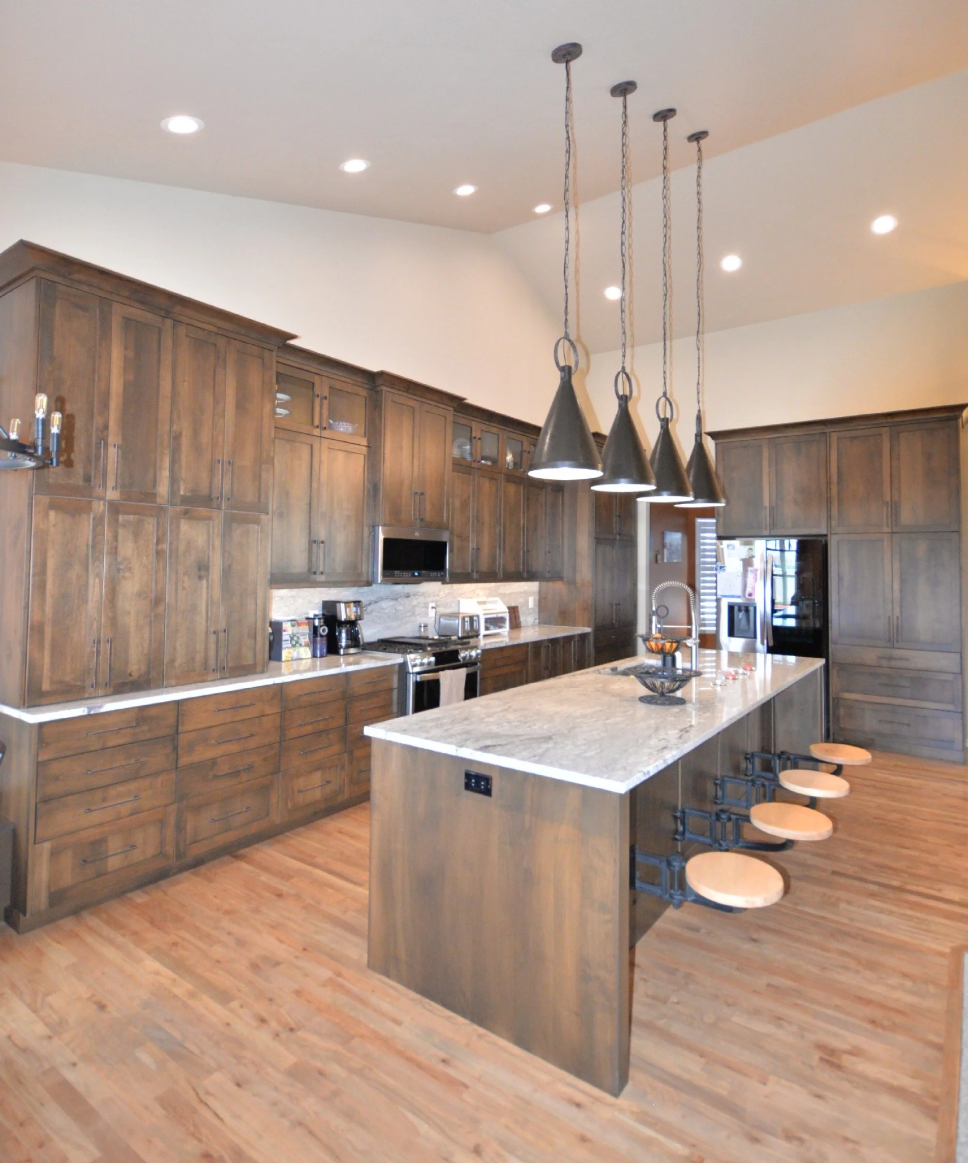 Stained wood kitchen cabinets with pull-out bar seats. Quarts countertop and light hardwood flooring.